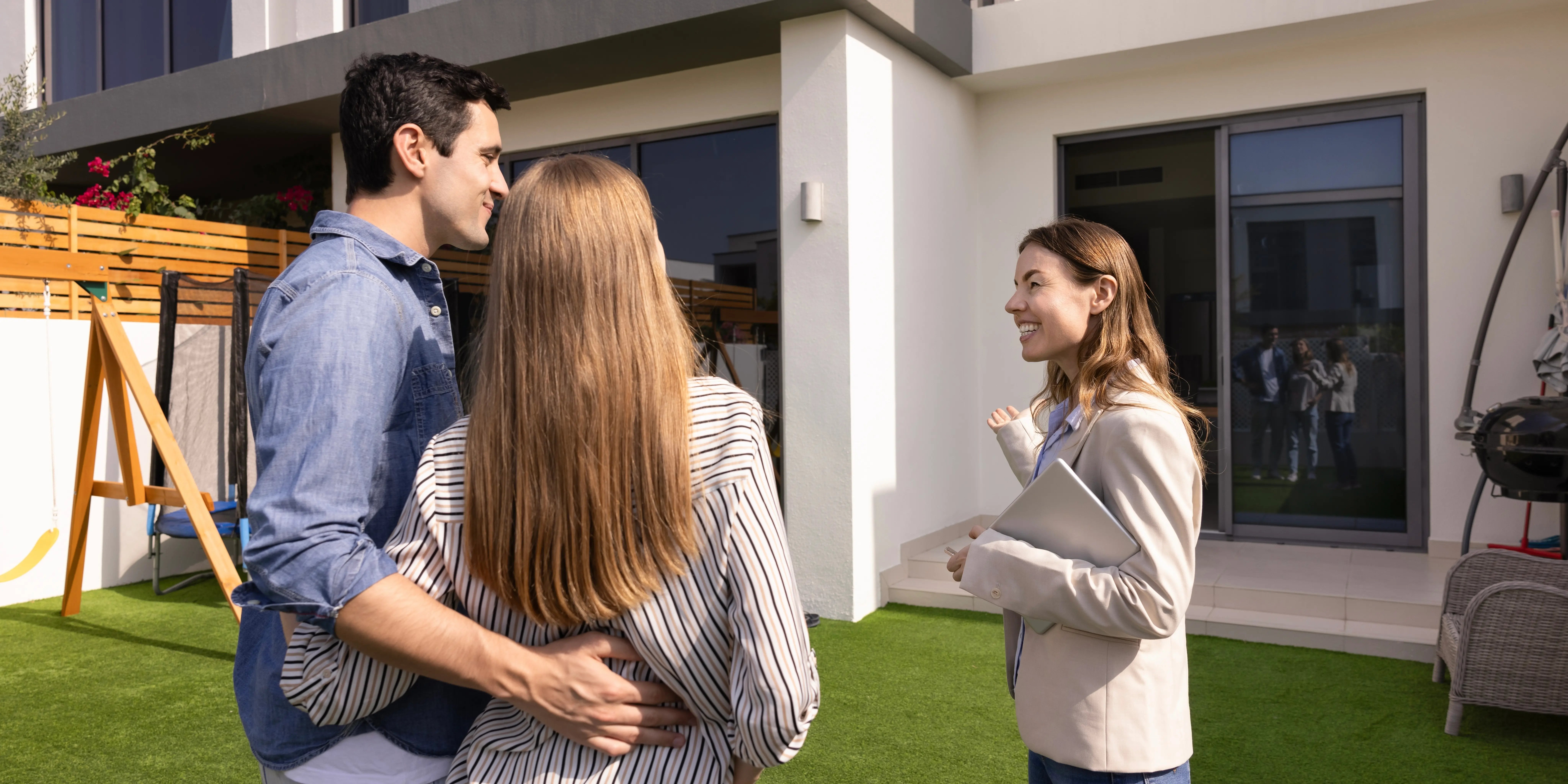 Agente de bienes raíces que muestra una casa para la venta a una pareja joven de Clientes, están de pie en el patio, apuntando el interior de la casa para recorrerla y conocer su estado