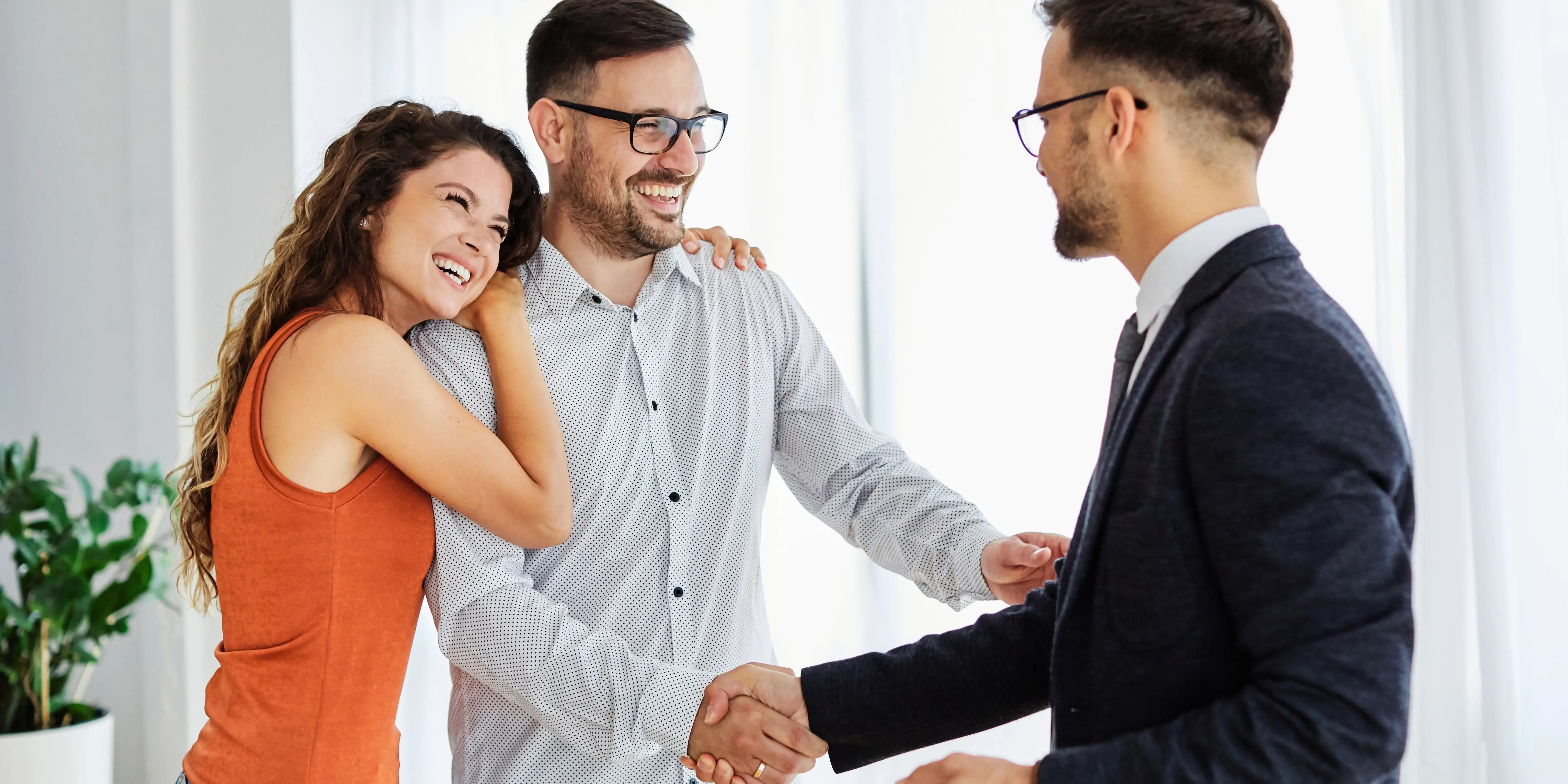 Agente inmobiliario estrechando la mano de pareja joven que acaba de comprar su casa con el ahorro del Infonavit