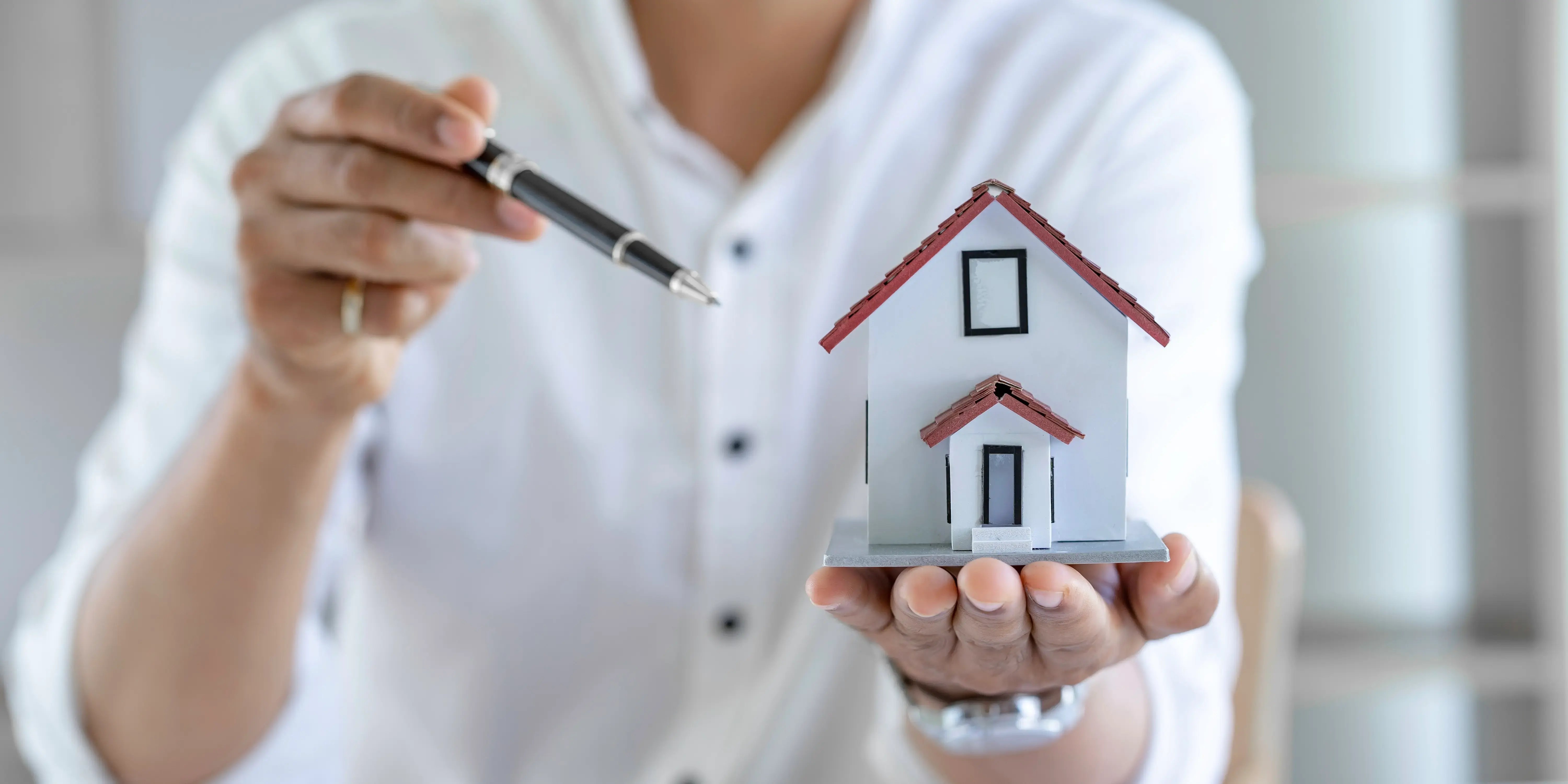 Agente inmobiliario sosteniendo una casa de madera y una pluma explicando como funciona un crédito hipotecario