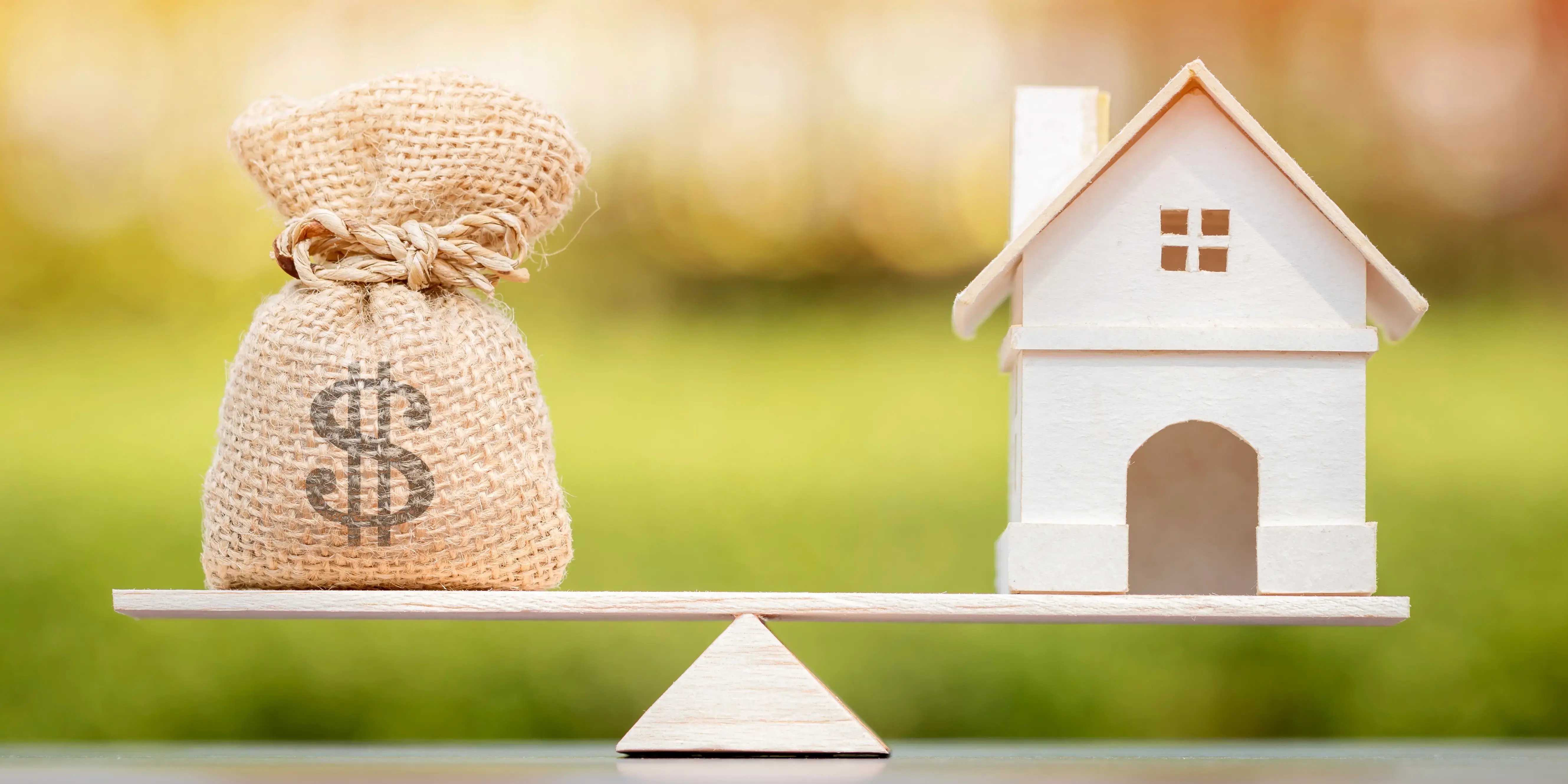 Balanza con un costal de dinero del lado izquierdo y una casa de madera del lado derecho haciendo referencia a comprar casa casi sin dinero