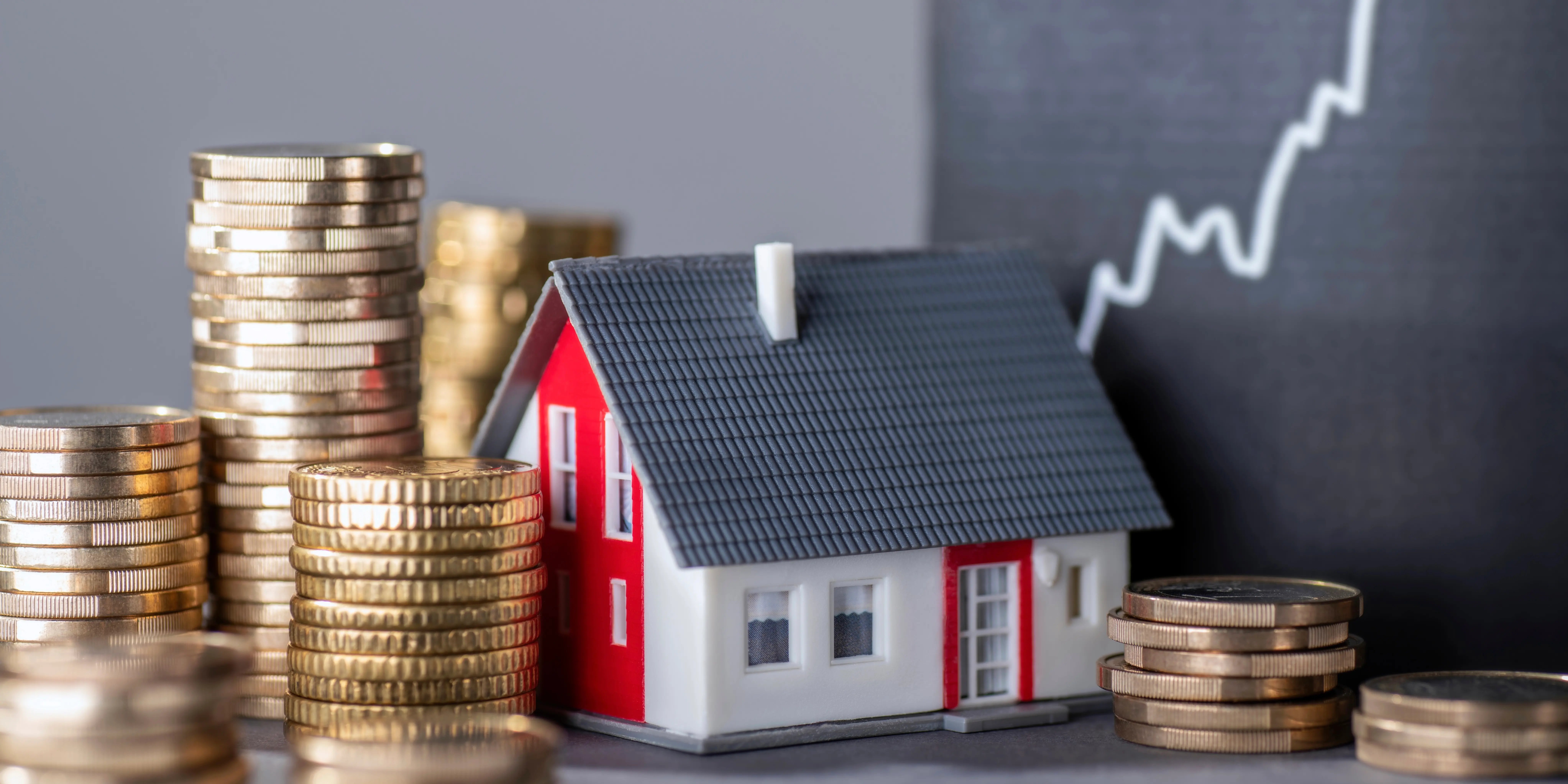 Casa con torres de monedas y una gráfica con una curva en alza que simboliza el aumento de la plusvalía