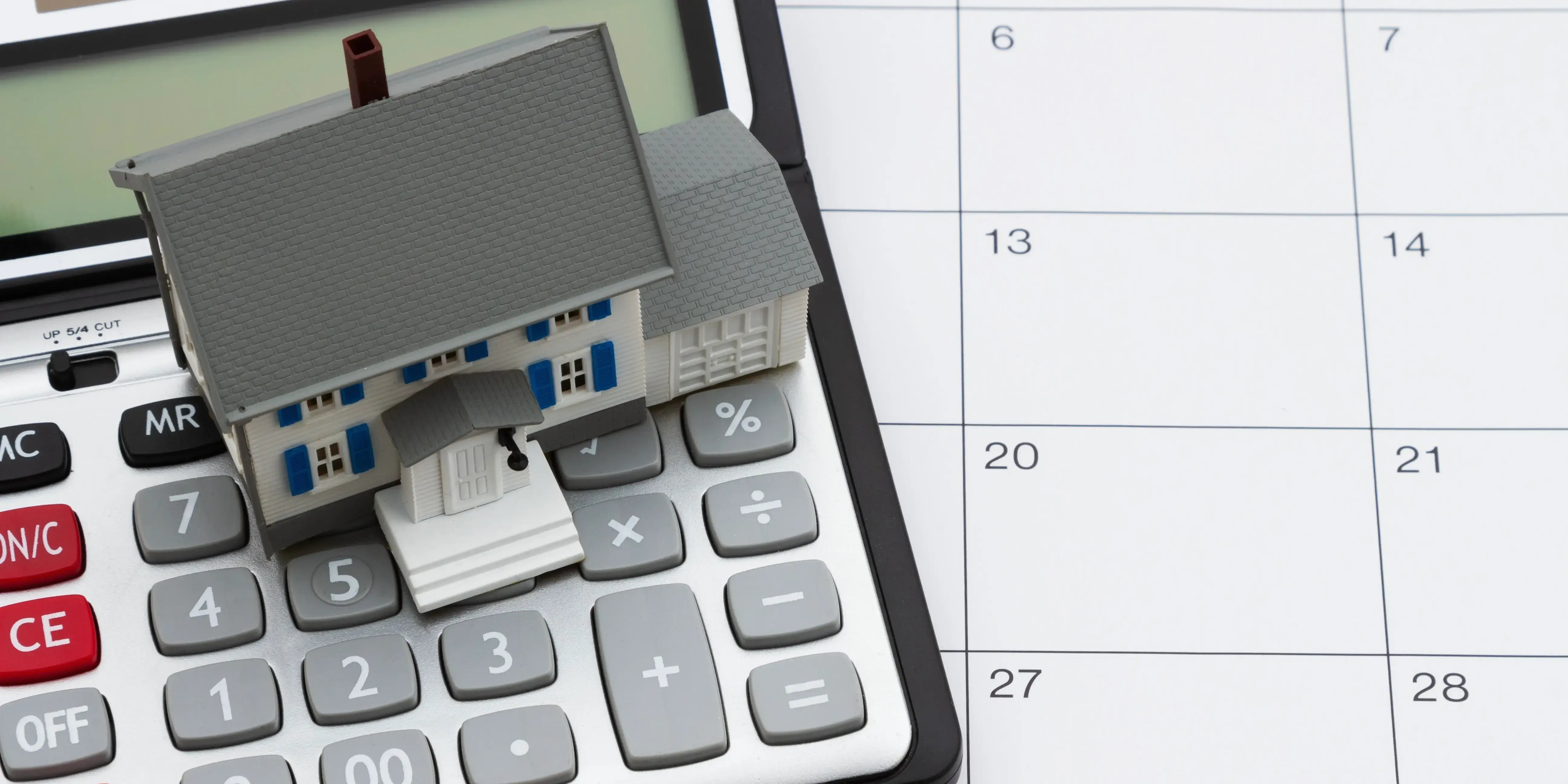 Casa de madera y una calculadora sobre un calendario donde se anotan las mensualidades que se tienen que pagar del crédito conyugal FOVISSSTE