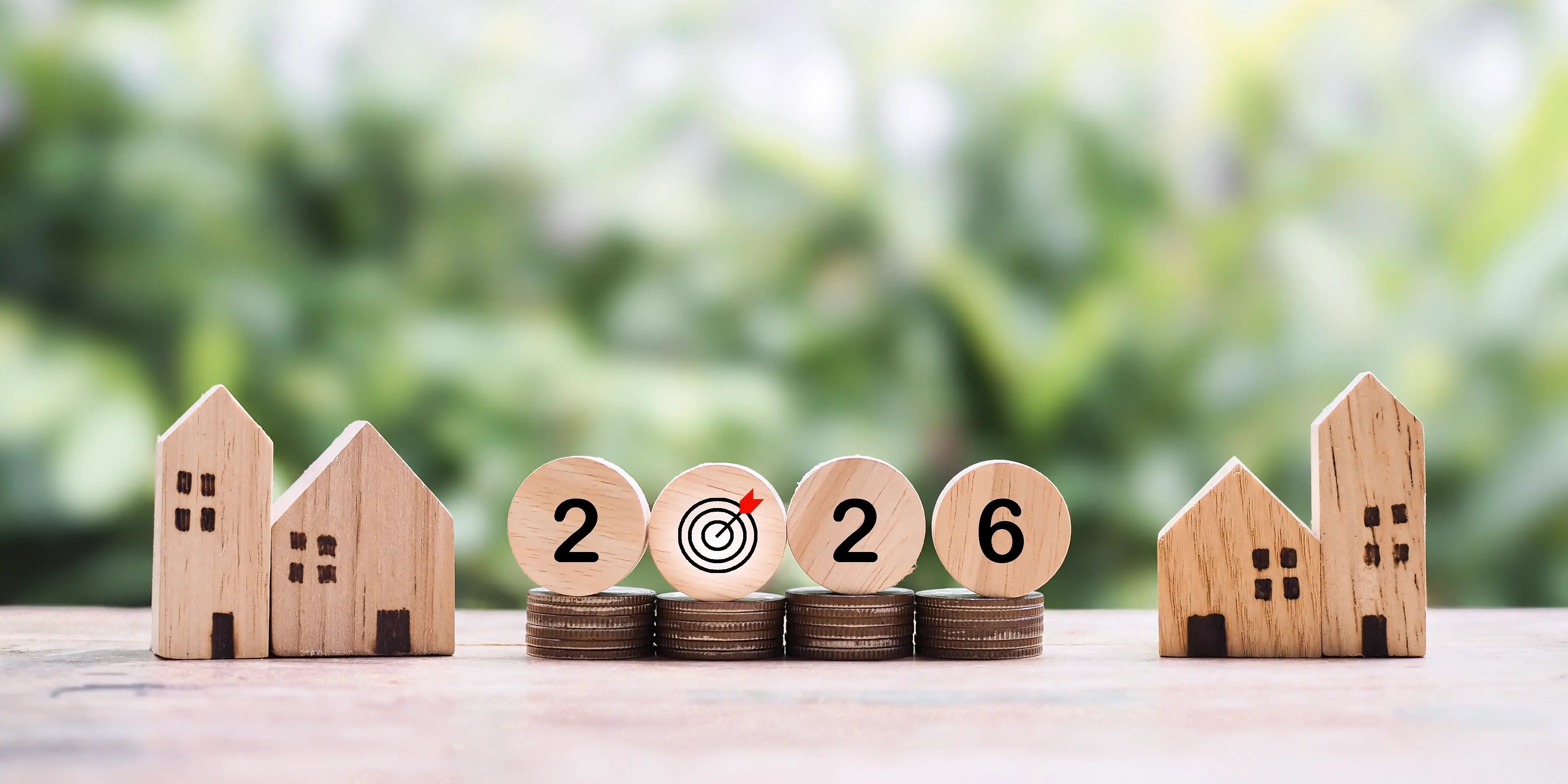 Casa en miniatura y bloques de madera con número 2026 en pila de monedas
