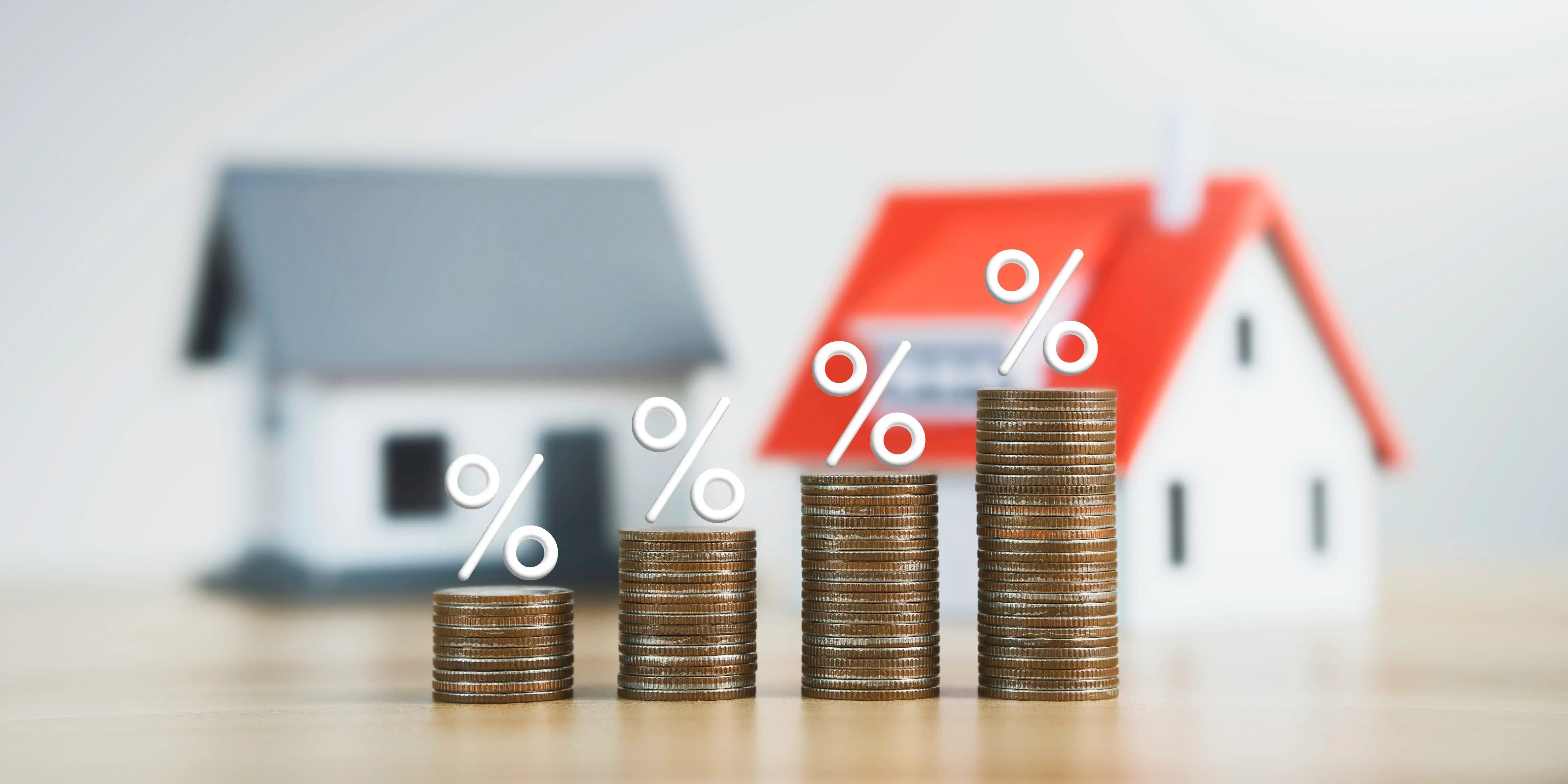 Dos casas de madera y al frente unas torres de monedas con símbolo de porcentaje por la tasa de interés para pagar una casa con crédito Infonavit