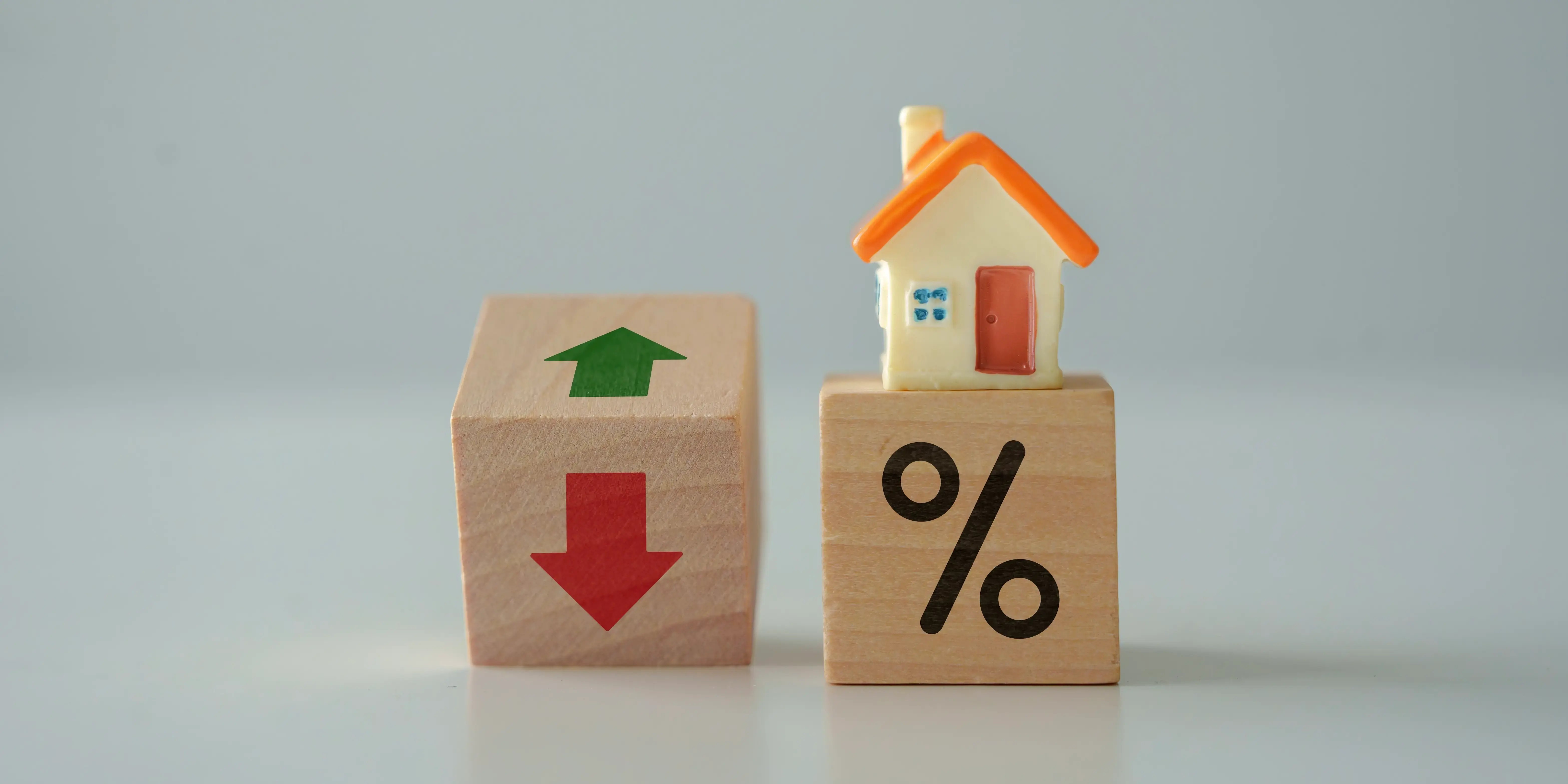 Dos cubos de madera, uno con el signo de porcentaje y una casa de juguete encima, el otro cubo con 2 flechas, una roja y una verde haciendo notar las ventajas y desventajas de la hipoteca a tipo fijo