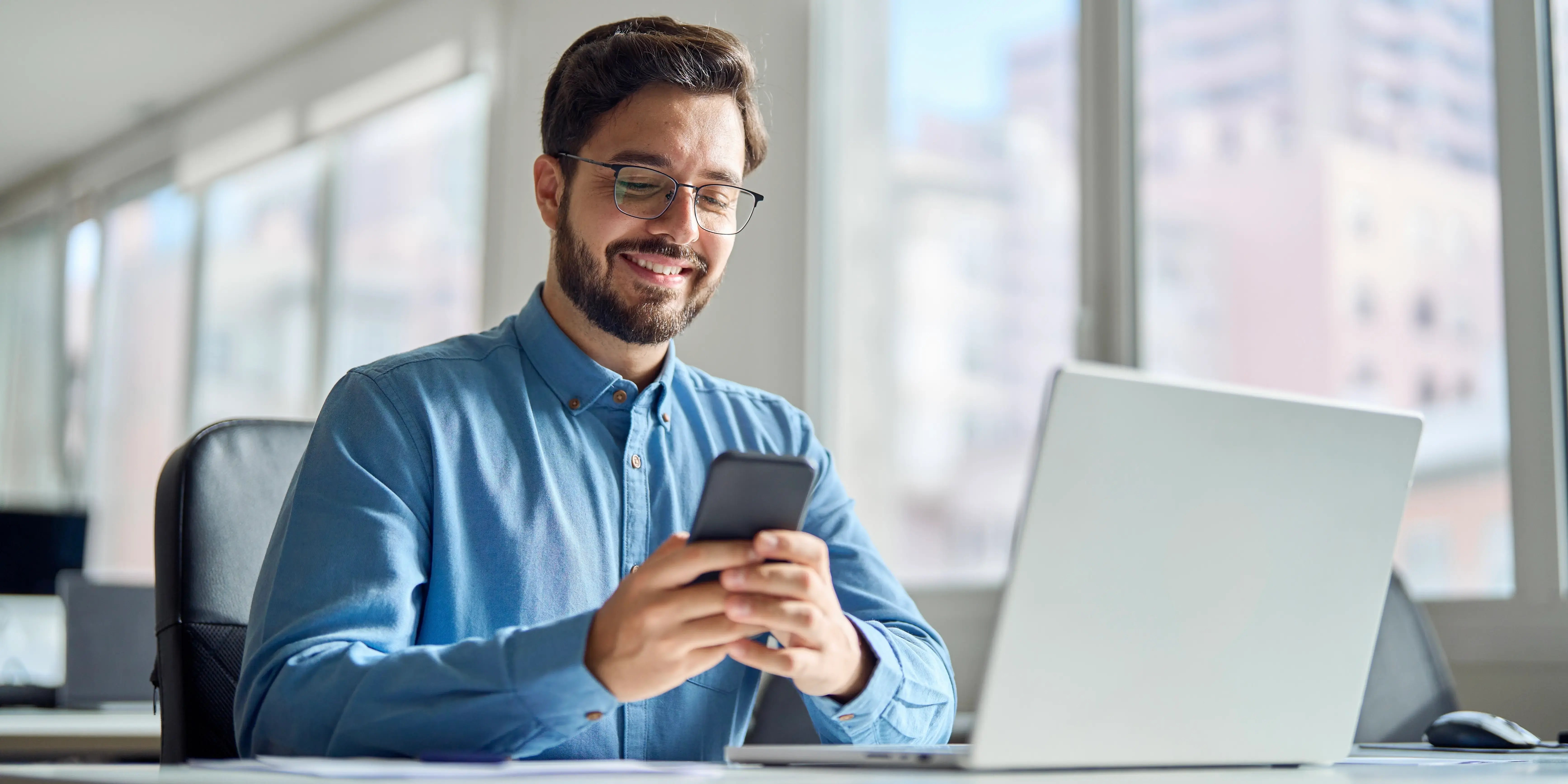 Hombre feliz en la oficina utilizando su smartphone y que compró casa cerca de su trabajo y ahorra tiempo en traslados