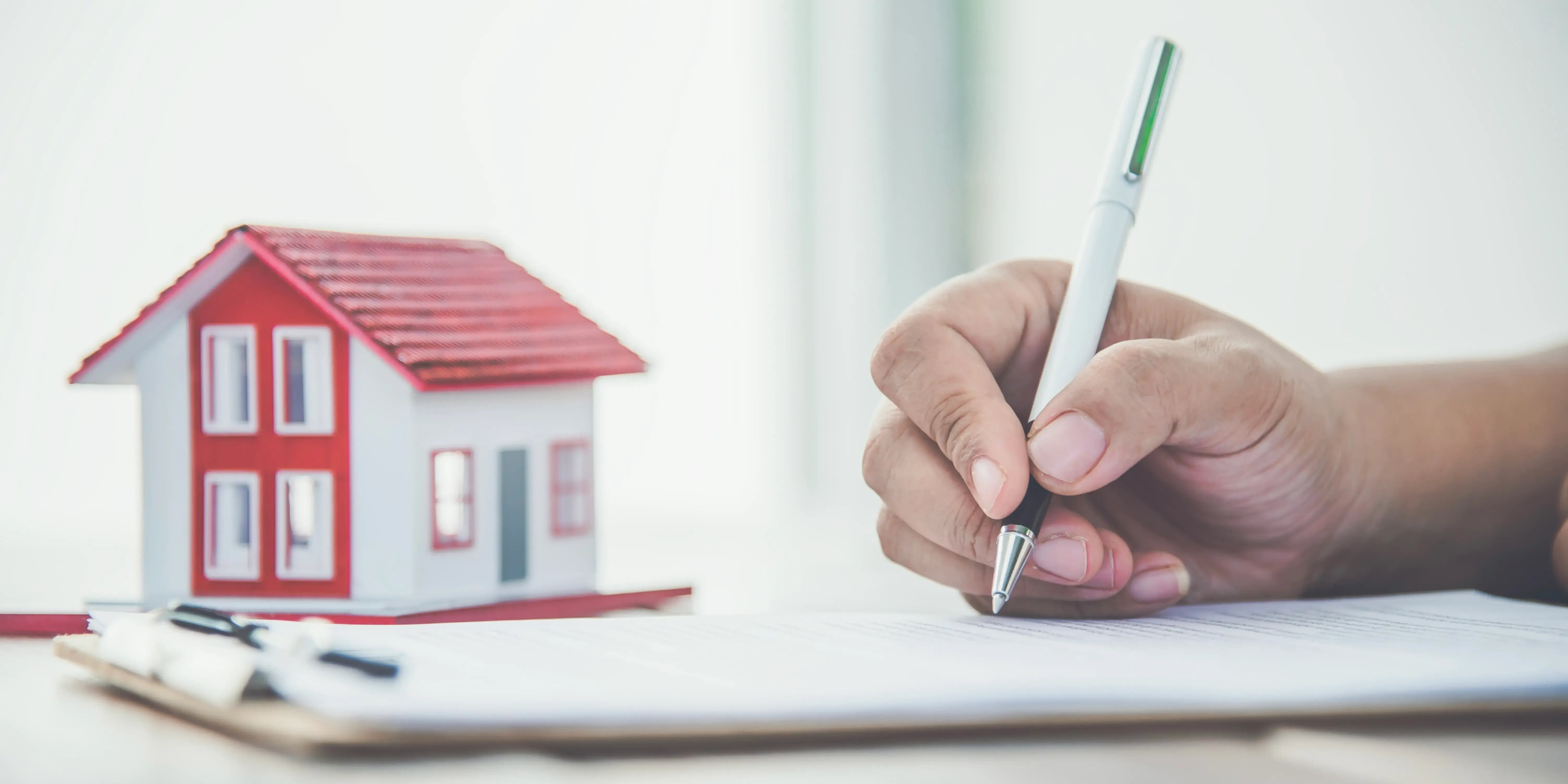 Hombre firmando unos papeles de su crédito Infonavit y al fondo se ve una casa de madera