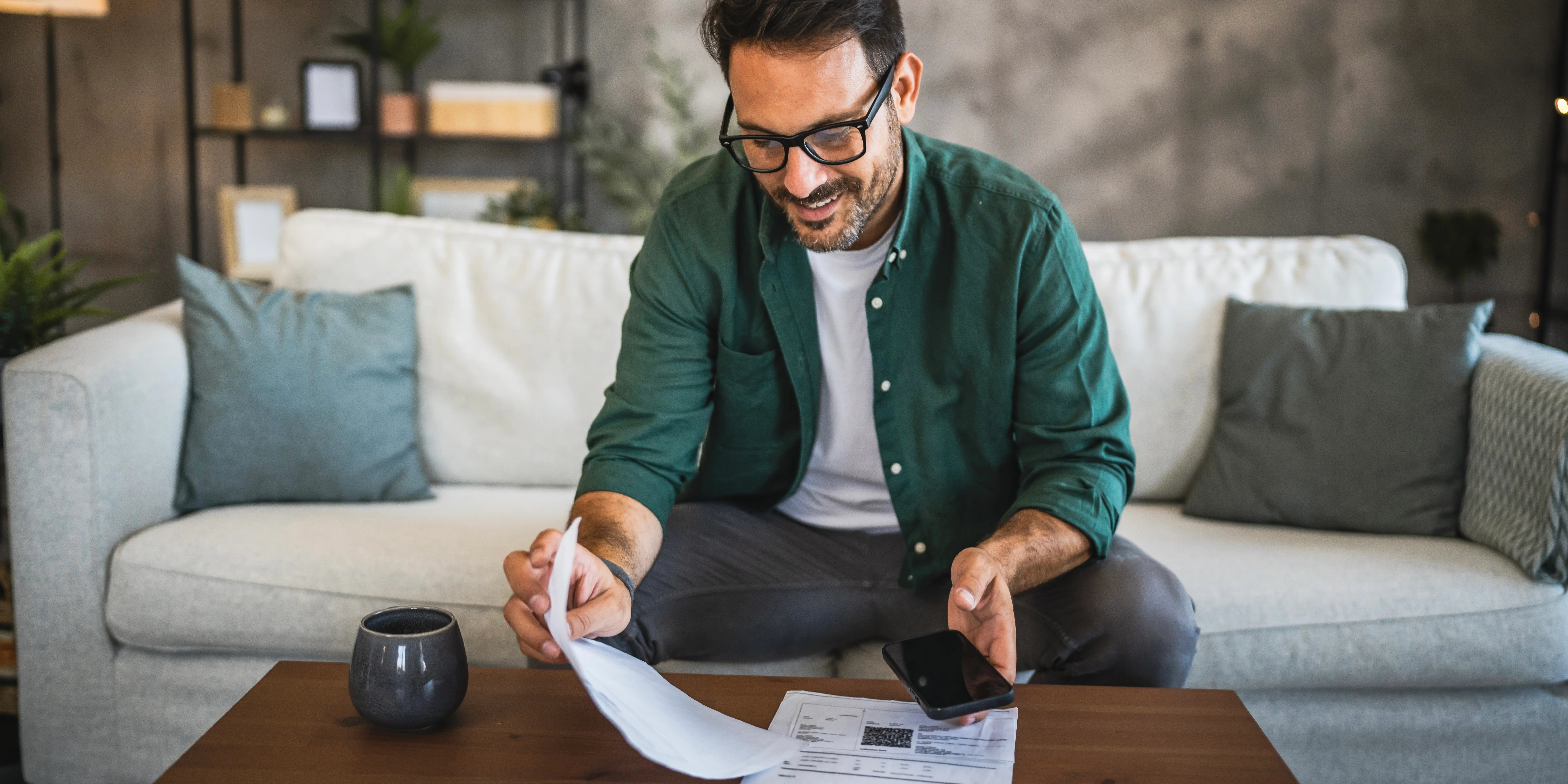 Hombre sentado en el sillón de su sala revisando el estado de cuenta para ver el avance de cuánto le falta para pagar una casa con crédito Infonavit