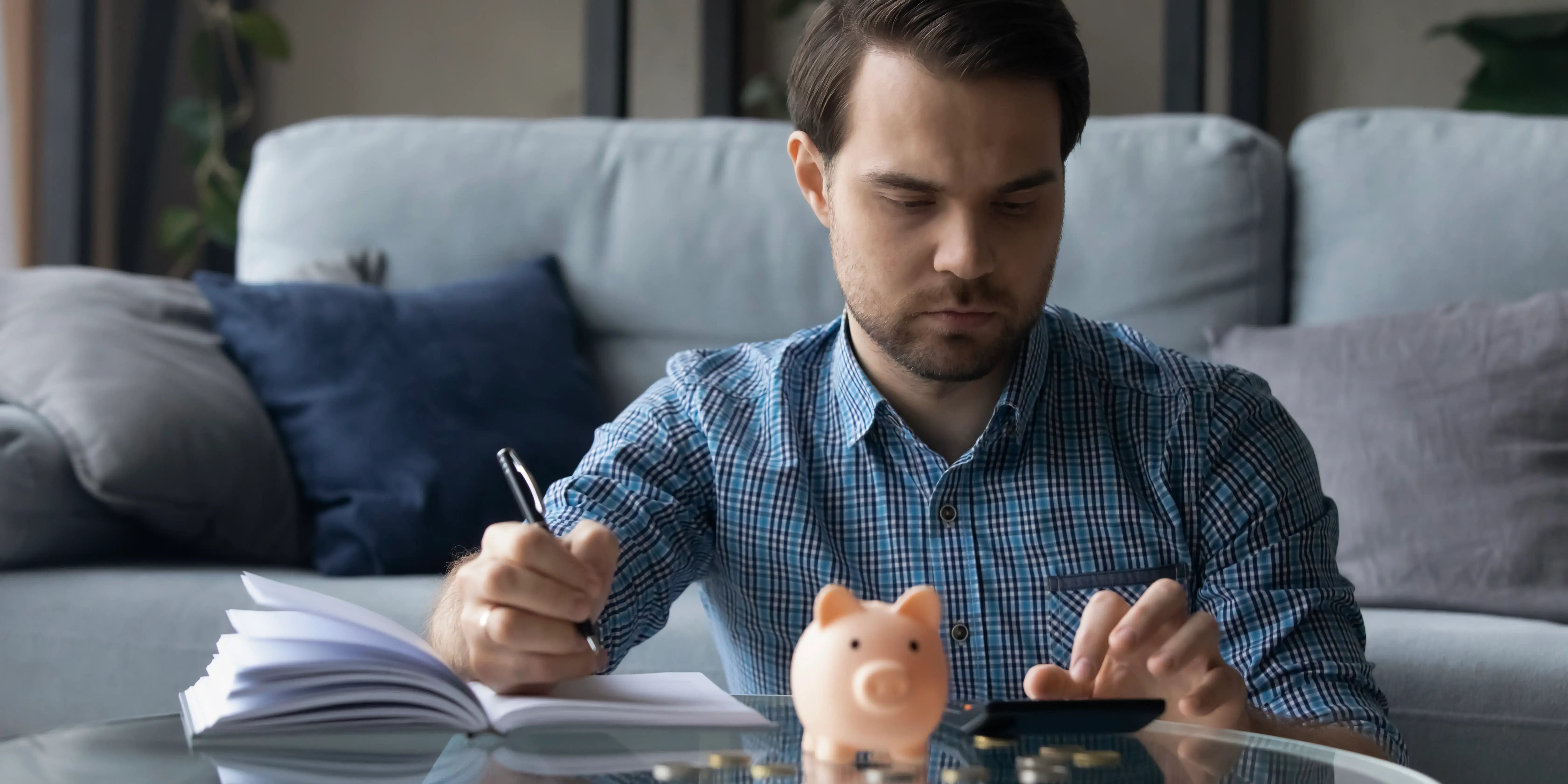 Hombre sentado en la sala con una libreta y una calculadora calculando su plan de presupuesto personal