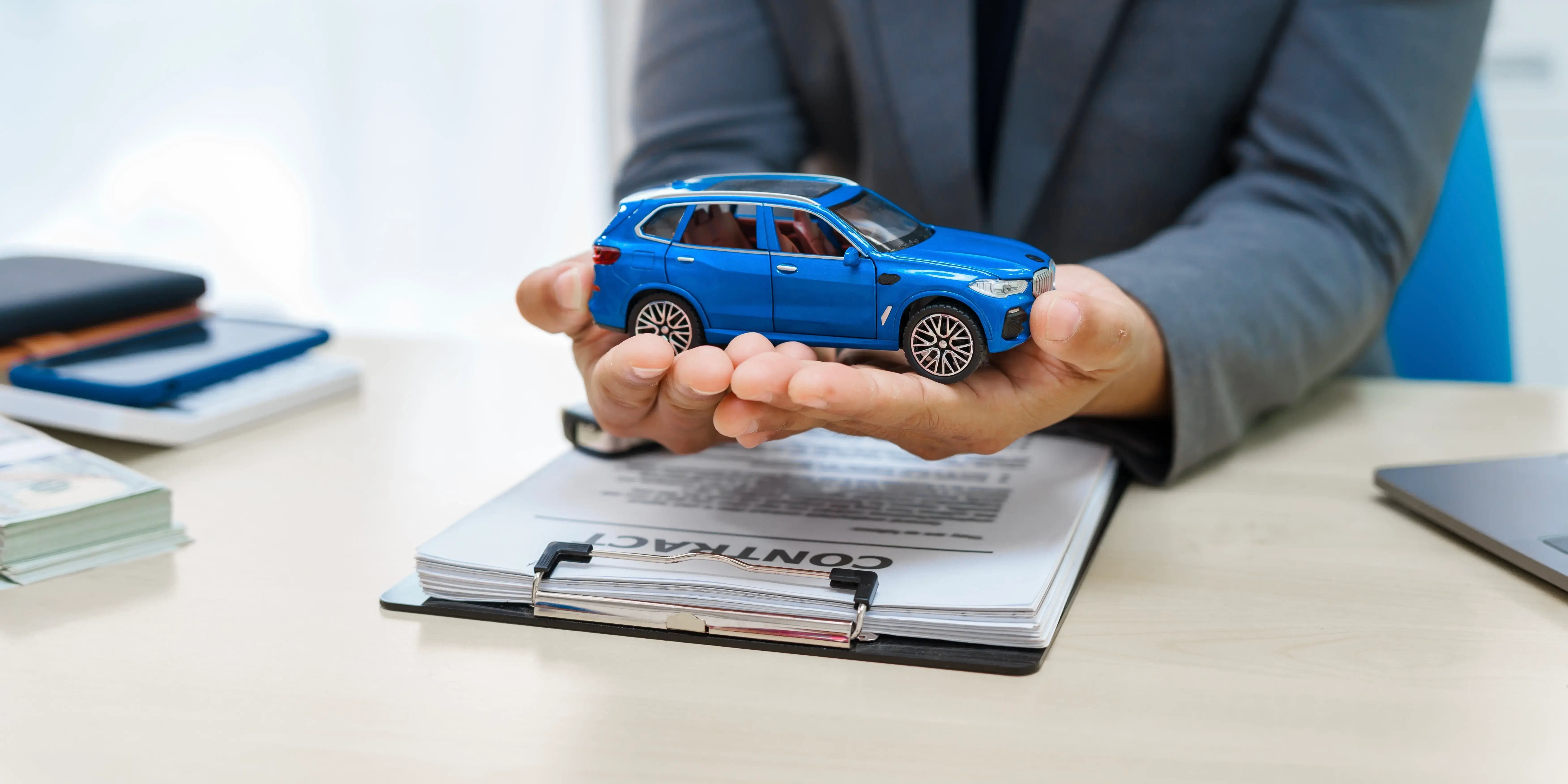 Hombre sosteniendo en las manos un coche azul de juguete y en el escritorio documentos para la firma del crédito automotriz