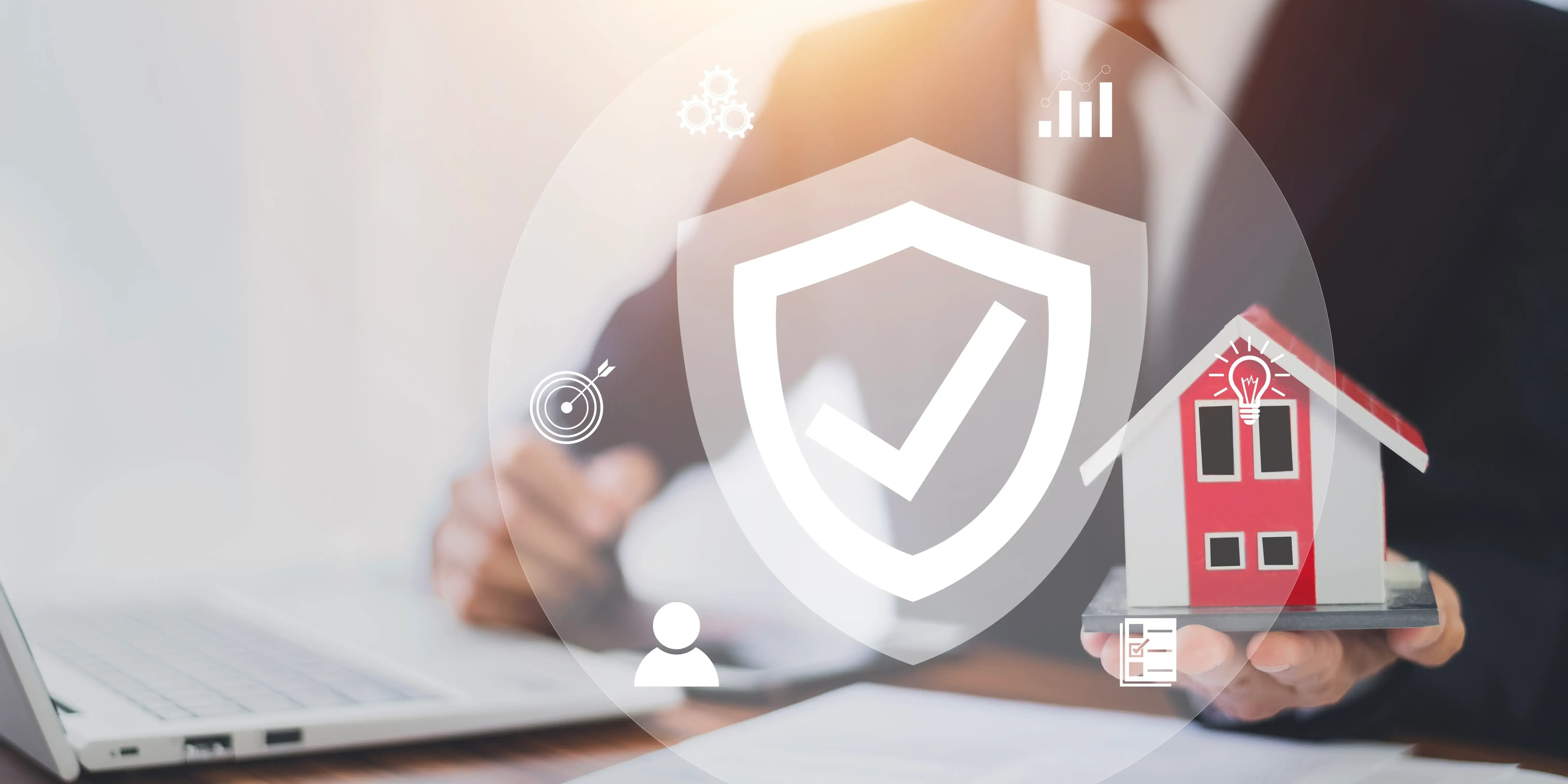 Hombre sosteniendo una casa roja de madera y utilizando una computadora para conocer el seguro de daños y proteger la vivienda mientras que se paga la casa con crédito Infonavit