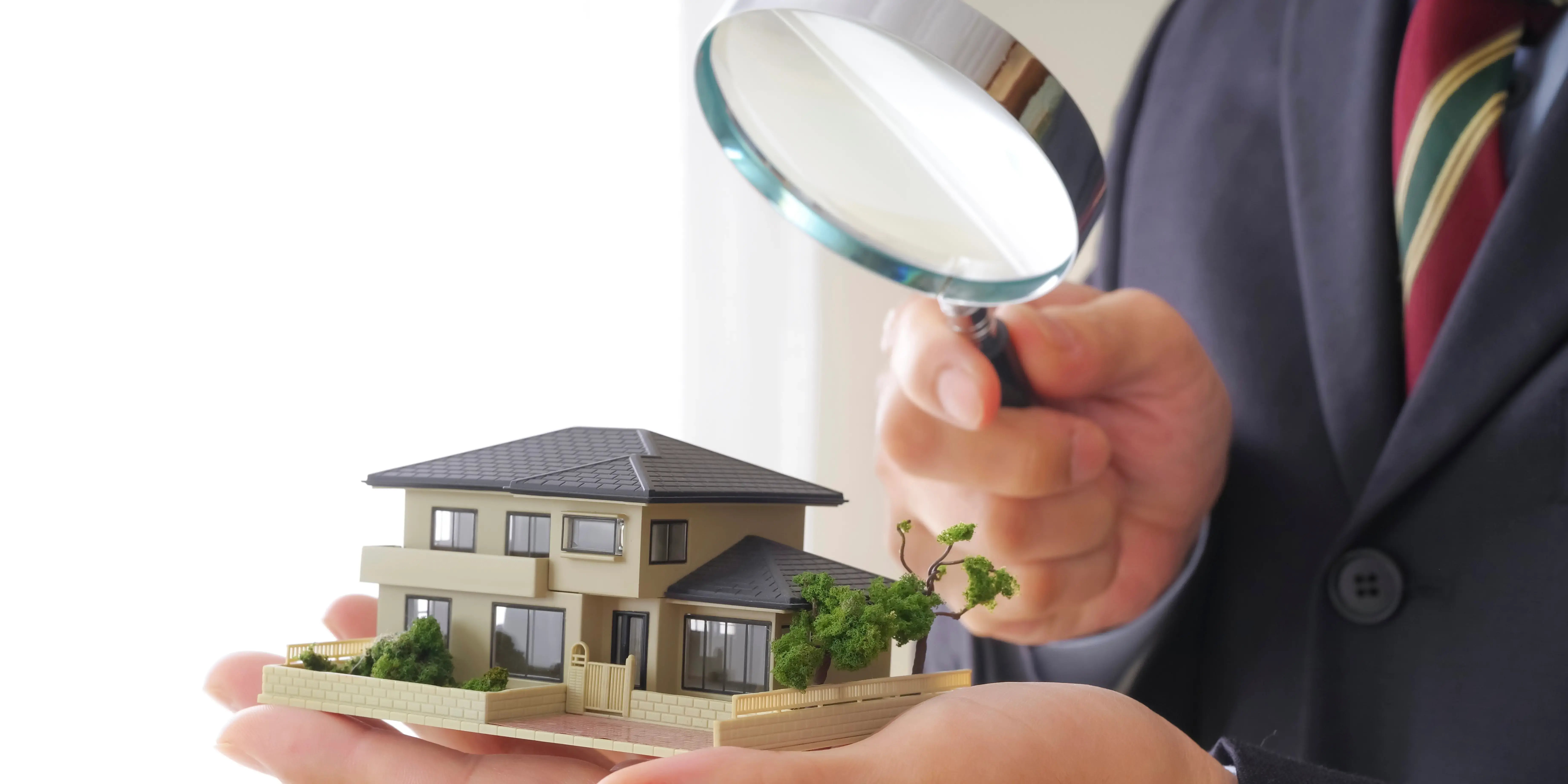 Hombre viendo con una lupa una casa de una maqueta para determinar los tipos de pusvalía que afectan la vivienda