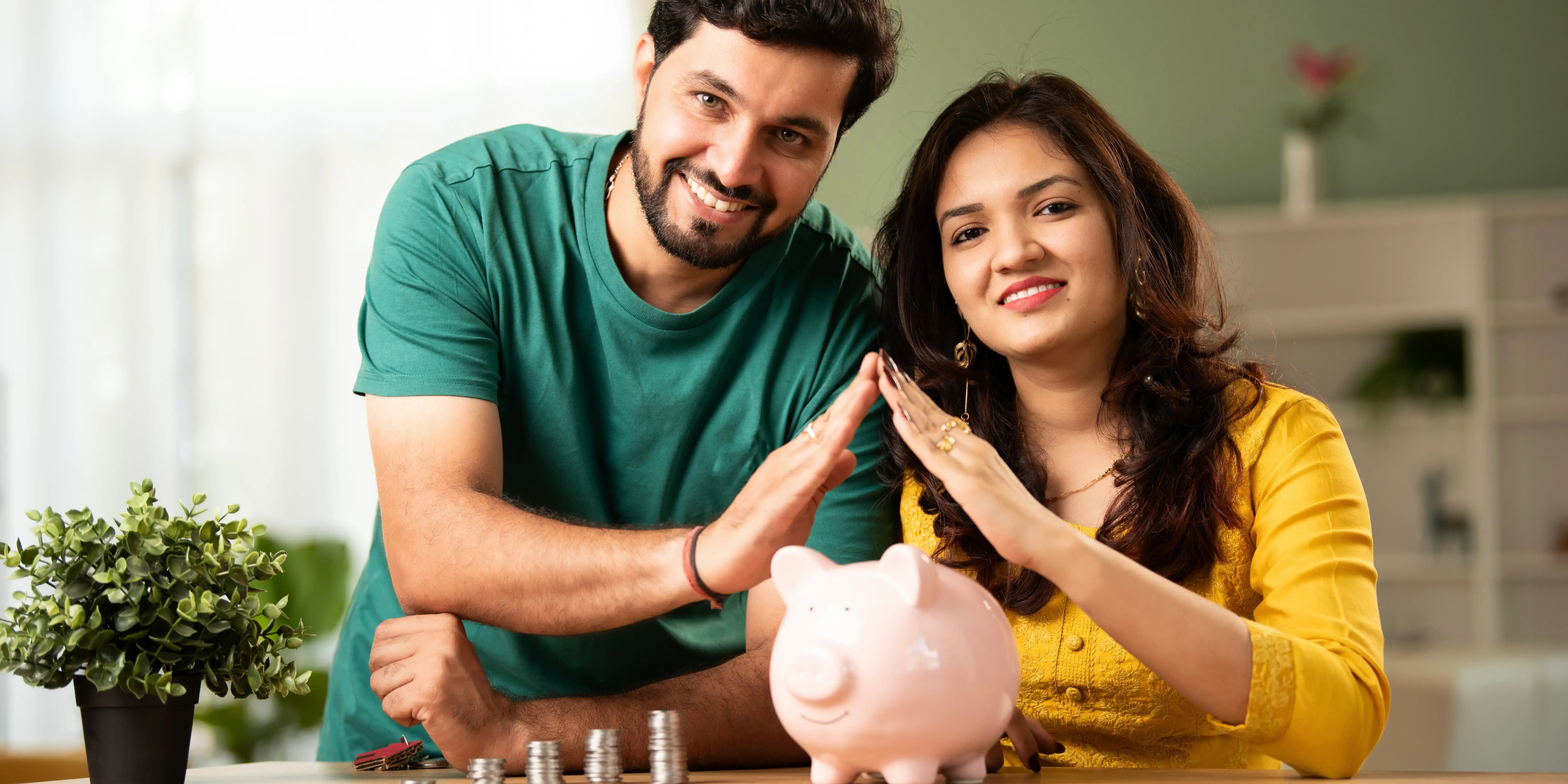 Hombre y mujer formando el techo de una casa con sus manos sobre una alcancía de puerco con ahorro del Infonavit