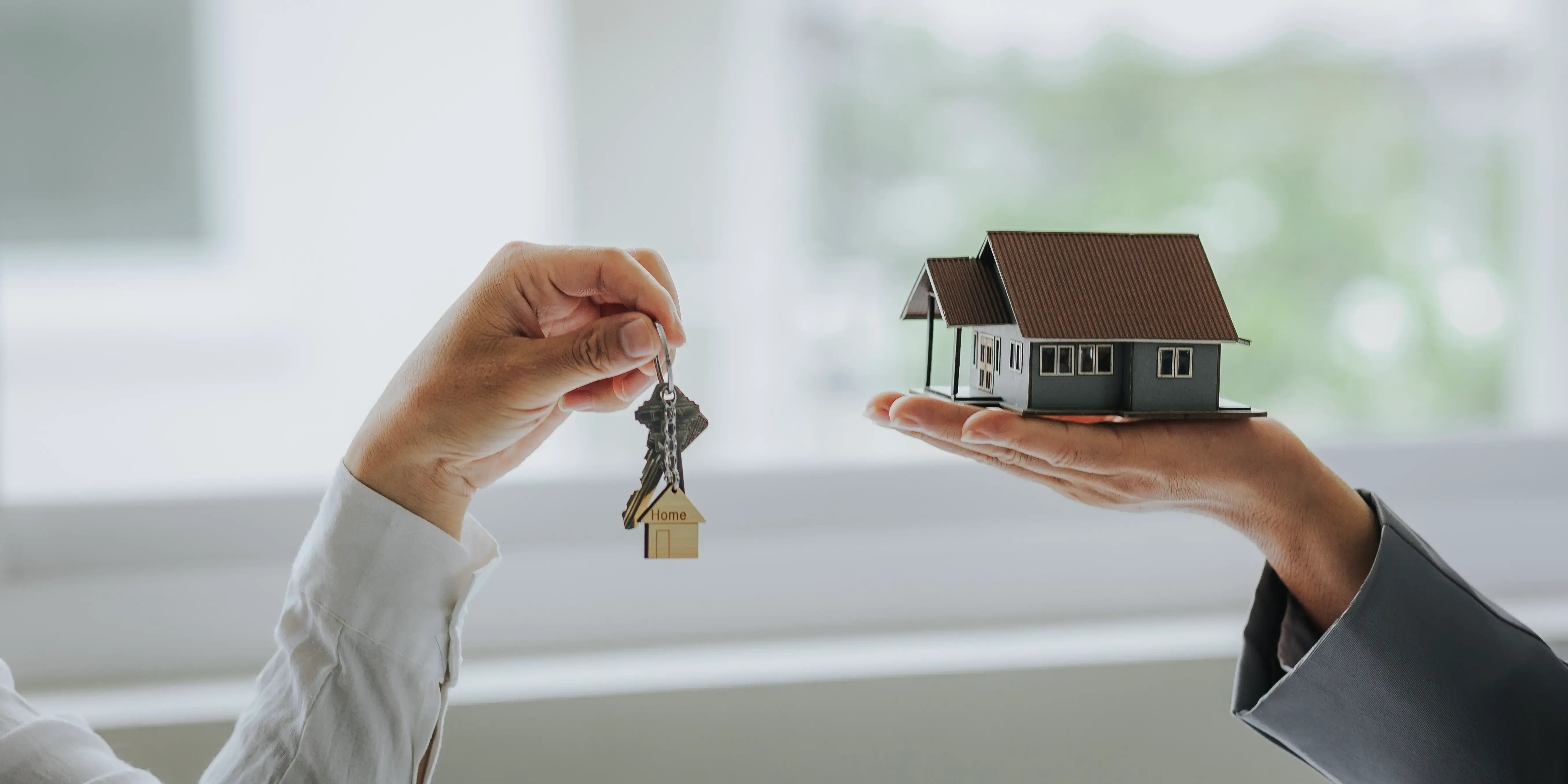 Manos de asesores inmobiliarios sosteniendo unas llaves y una casa respectivamente para comprar casa sin Infonavit