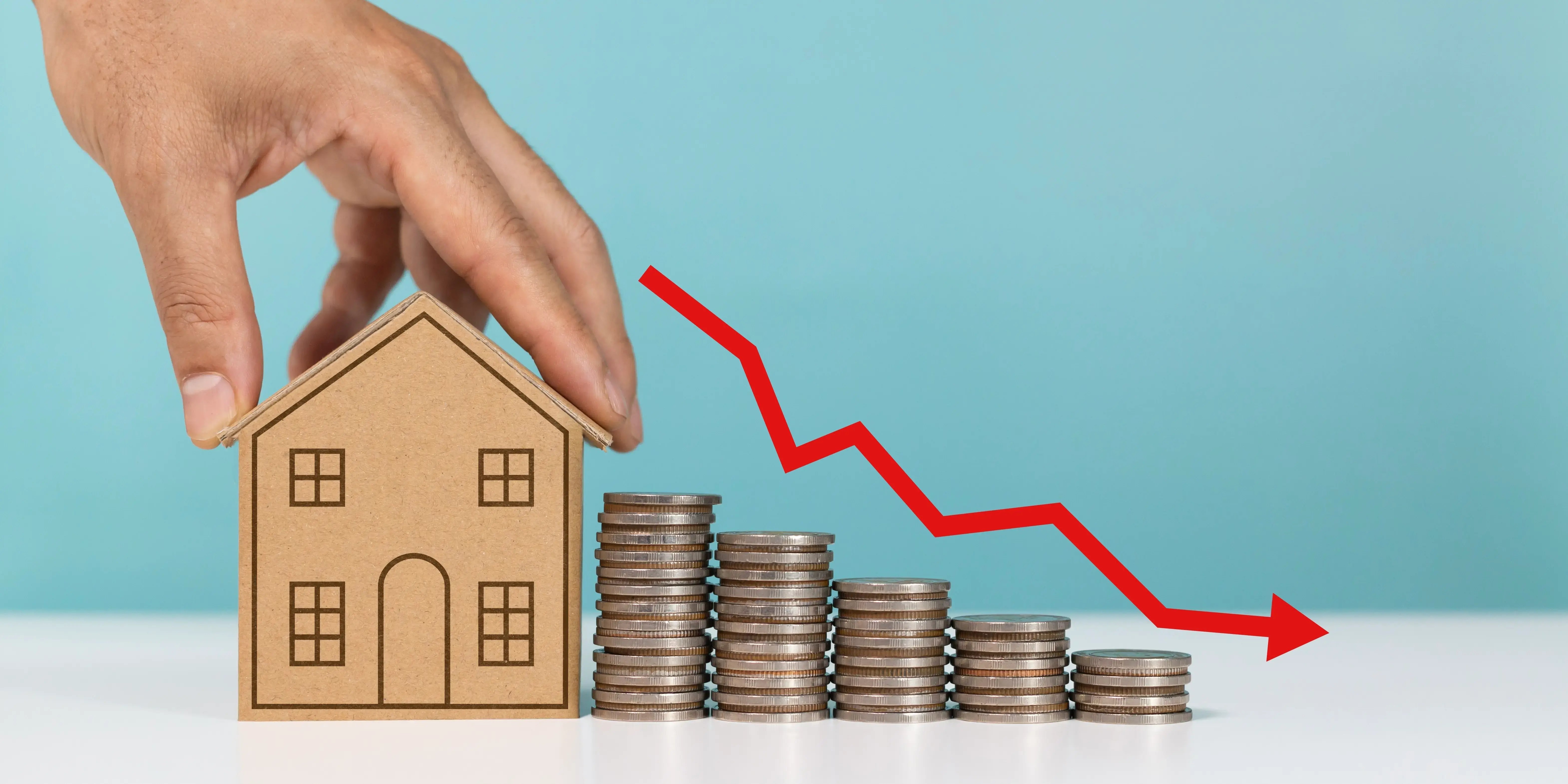 Mini casa modelo con pila de monedas y flecha hacia abajo de Indicando crédito hipotecario para vivienda accesible