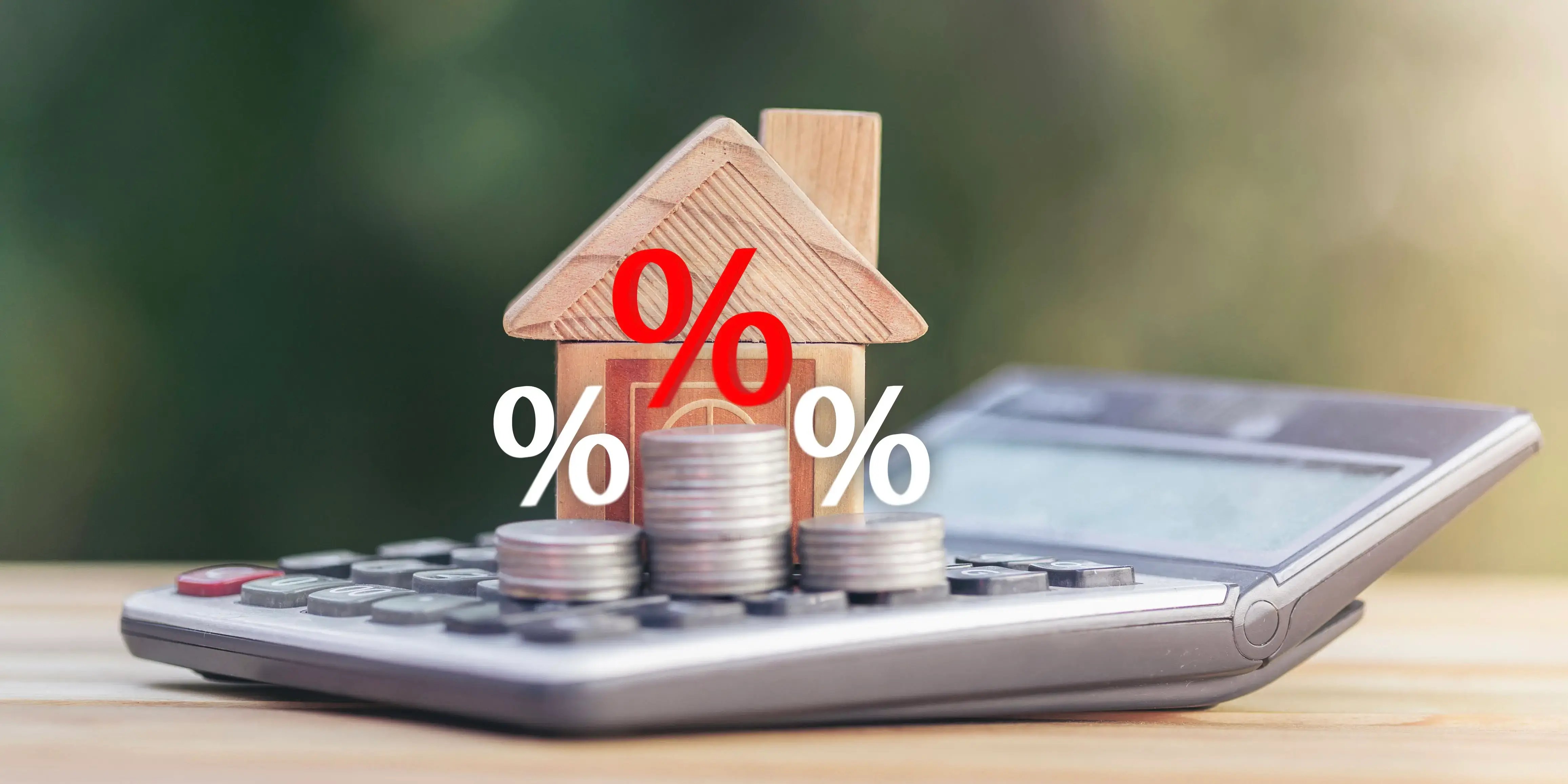 Monedas y casa de madera sobre una calculadora para calcular el factor de descuento Infonavit