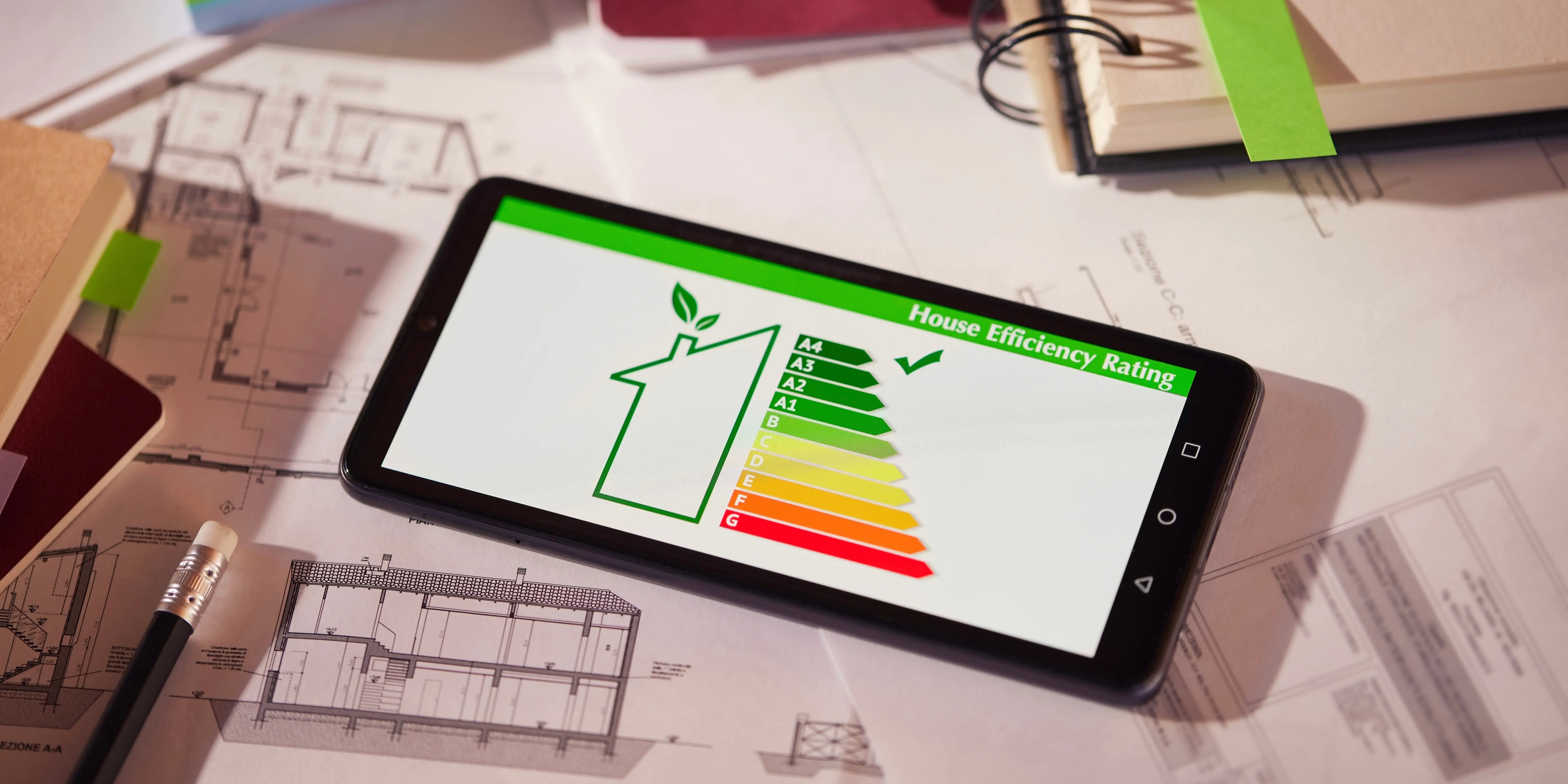 Pantalla de eficiencia energética en teléfono móvil que está sobre dibujos y planos de una nueva casa con certificación edge