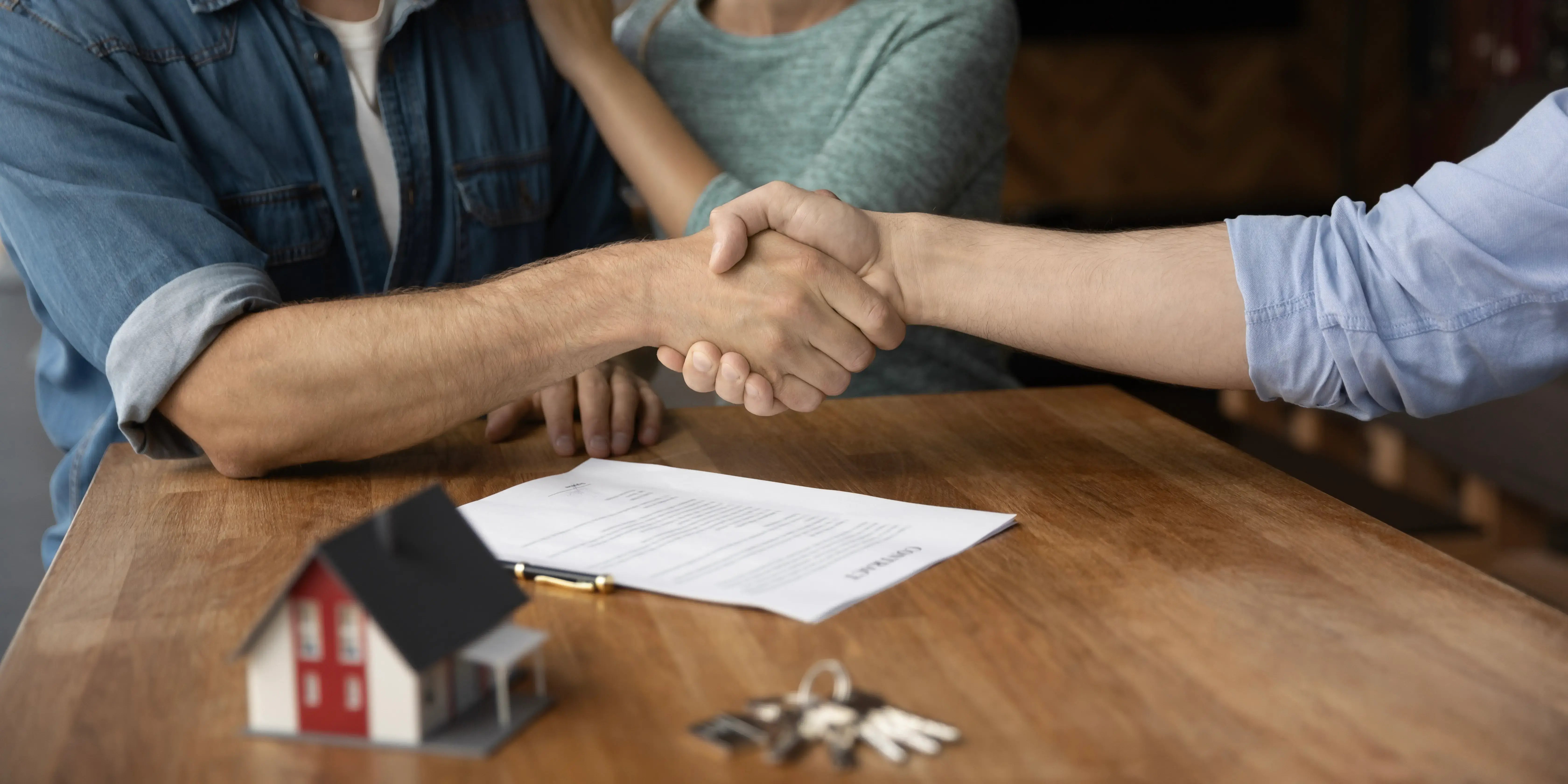 Pareja dando la mano a asesor hipotecario después de mejorar la condiciones para comprar una casa y ahorrar dinero