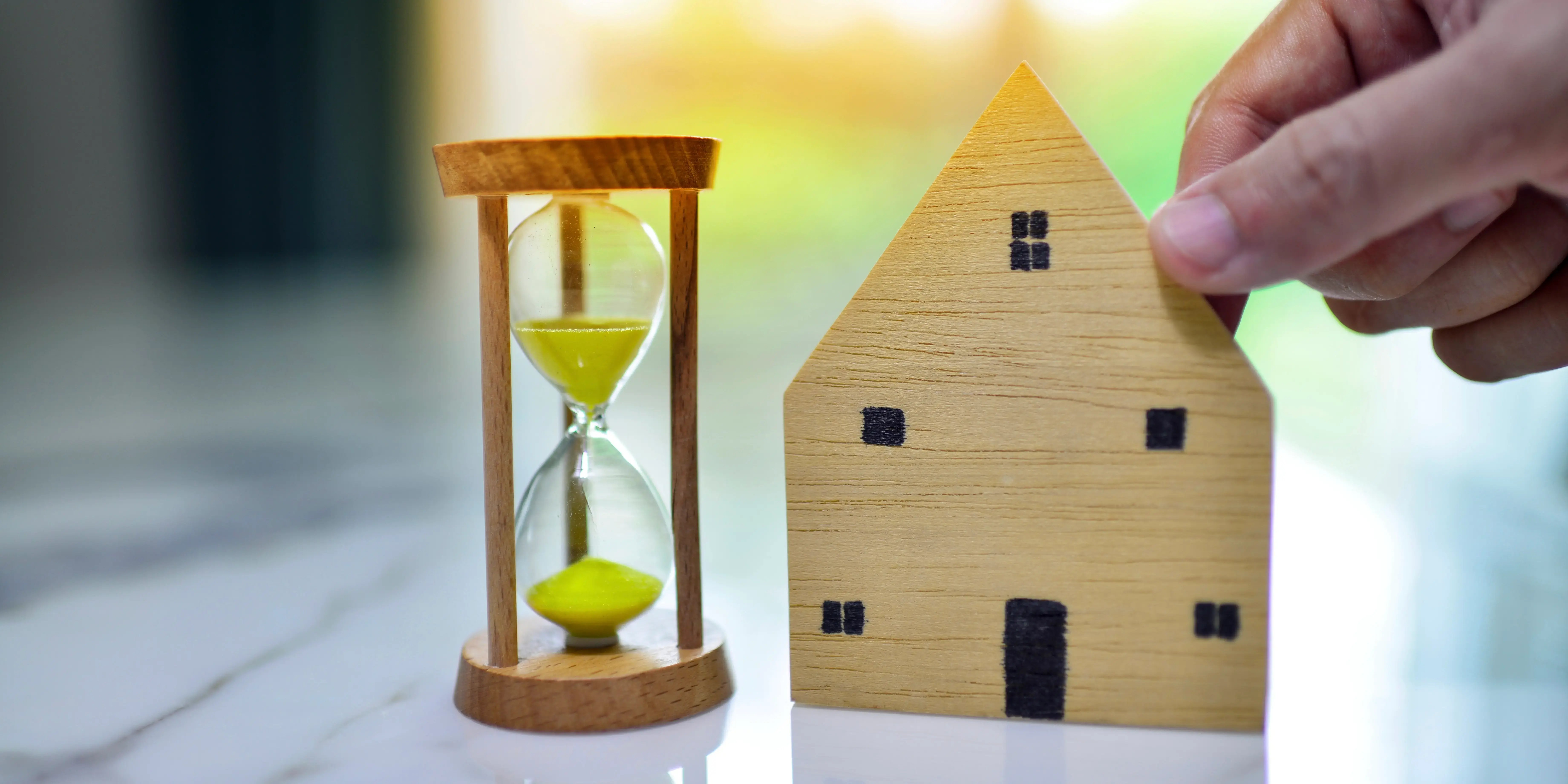 Persona agarrando un mini modelo de casa de madera con un reloj de arena a un lado, eligiendo liquidar la hipoteca antes de tiempo