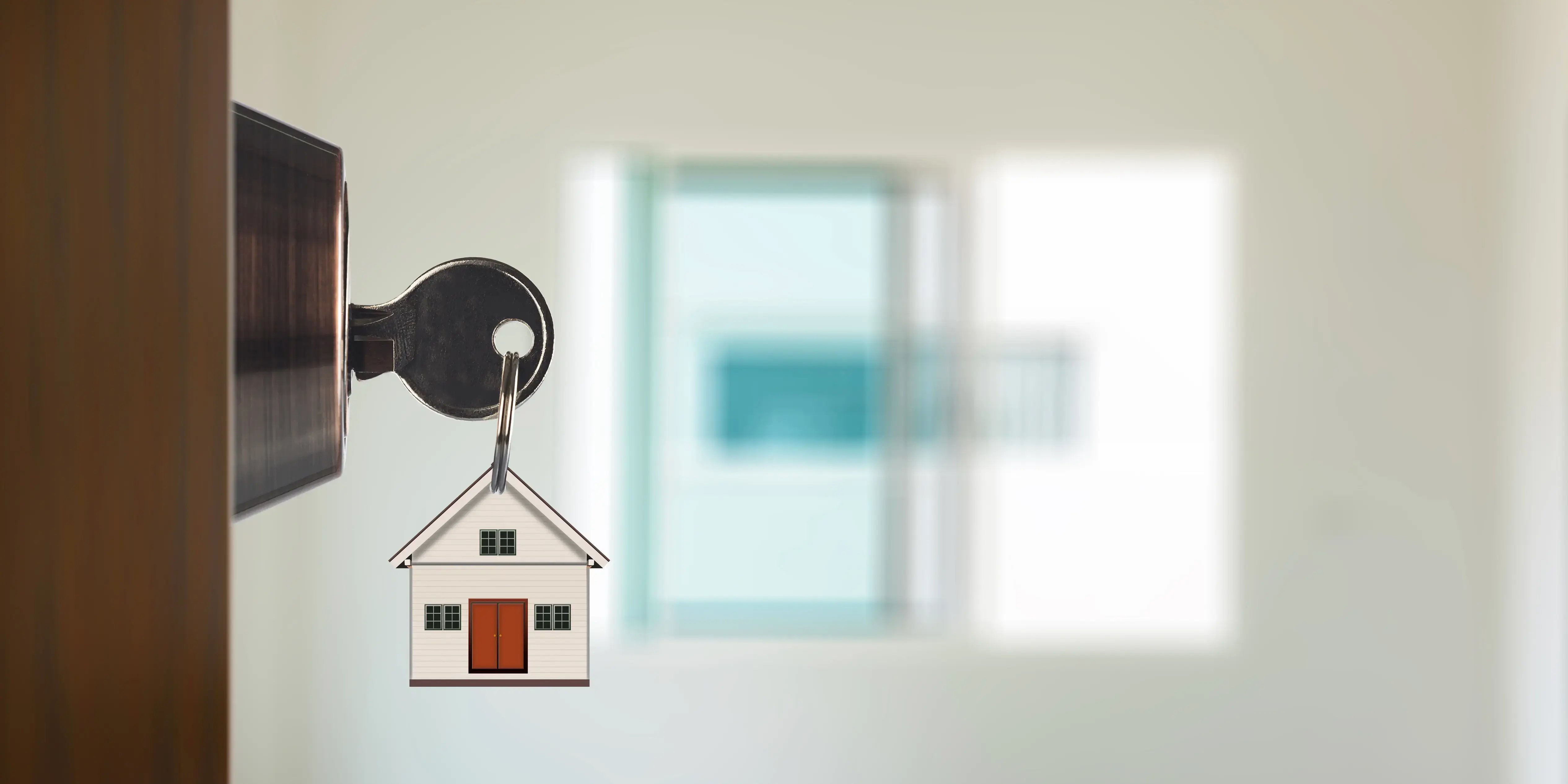 Puerta con las llaves de la casa en la cerradura, al fondo se ve un cuarto iluminado y una ventana de una vivienda adecuada para vivir
