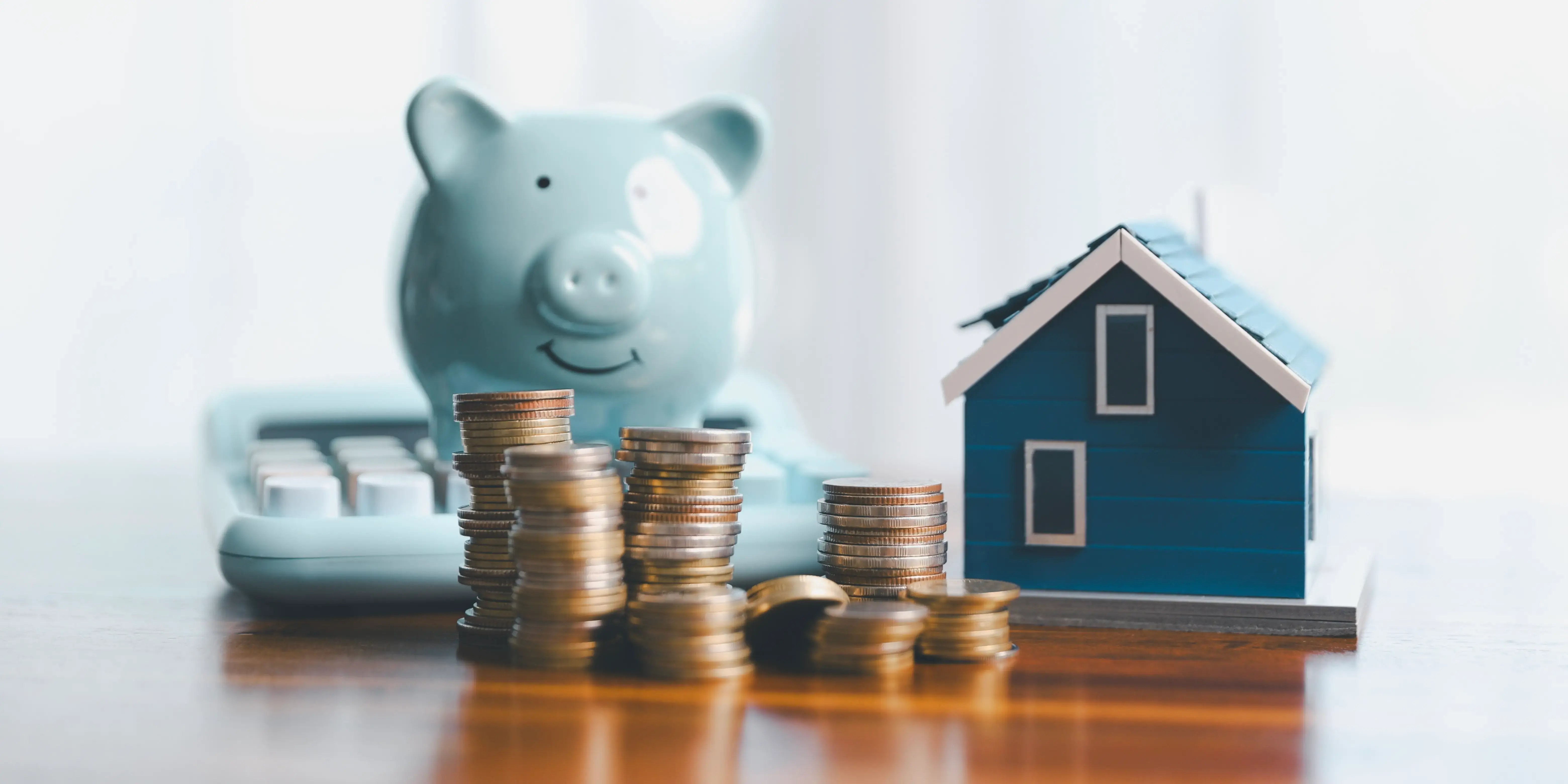 Torres de monedas, una casa de madera sobre una mesa y una alcancía de marrano para ahorrar para el enganche de una casa con un plan de presupuesto personal