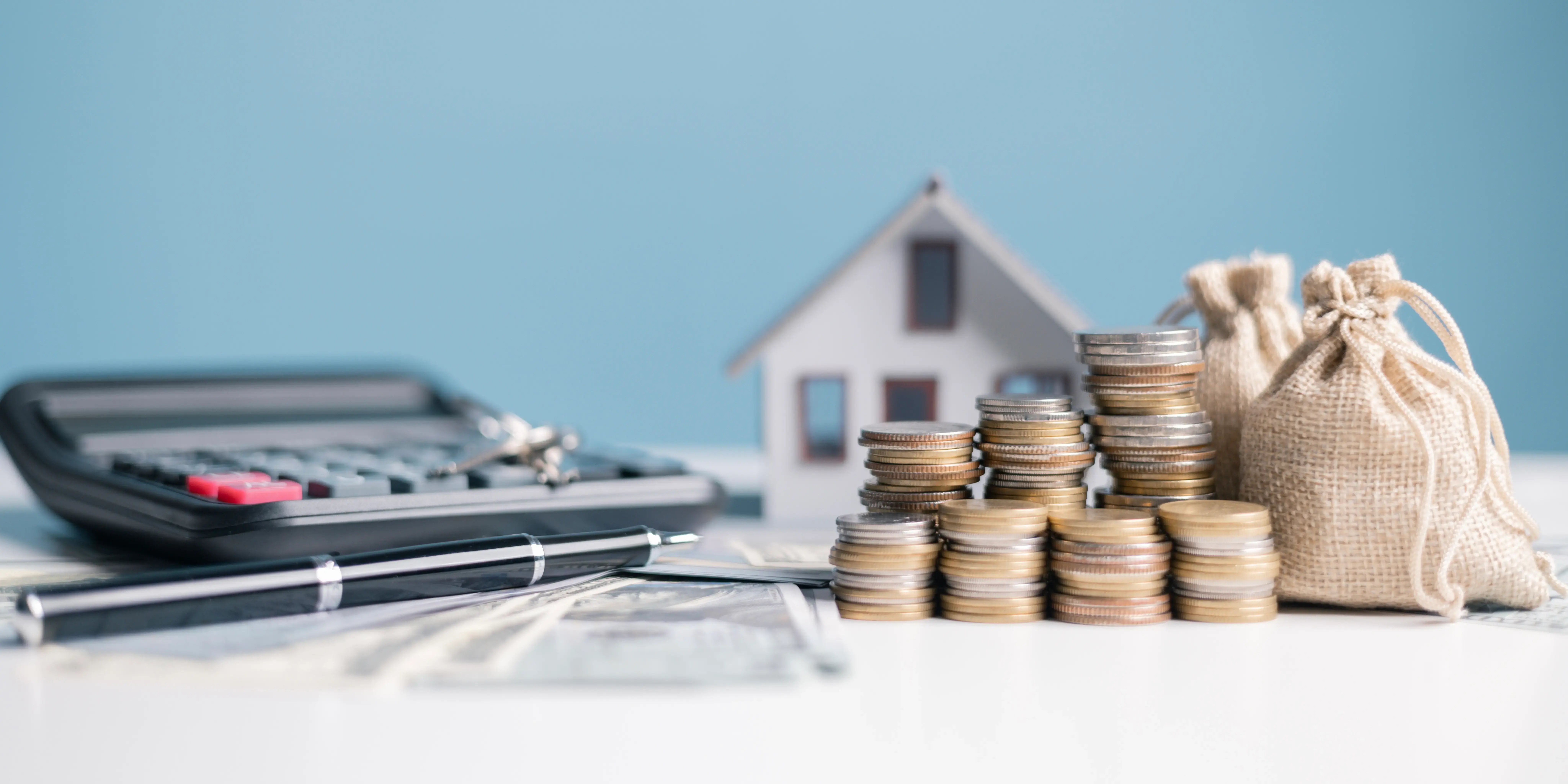 Una calculadora, una casa de madera y torres de monedas junto unos costales de dinero por el ahorro del infonavit