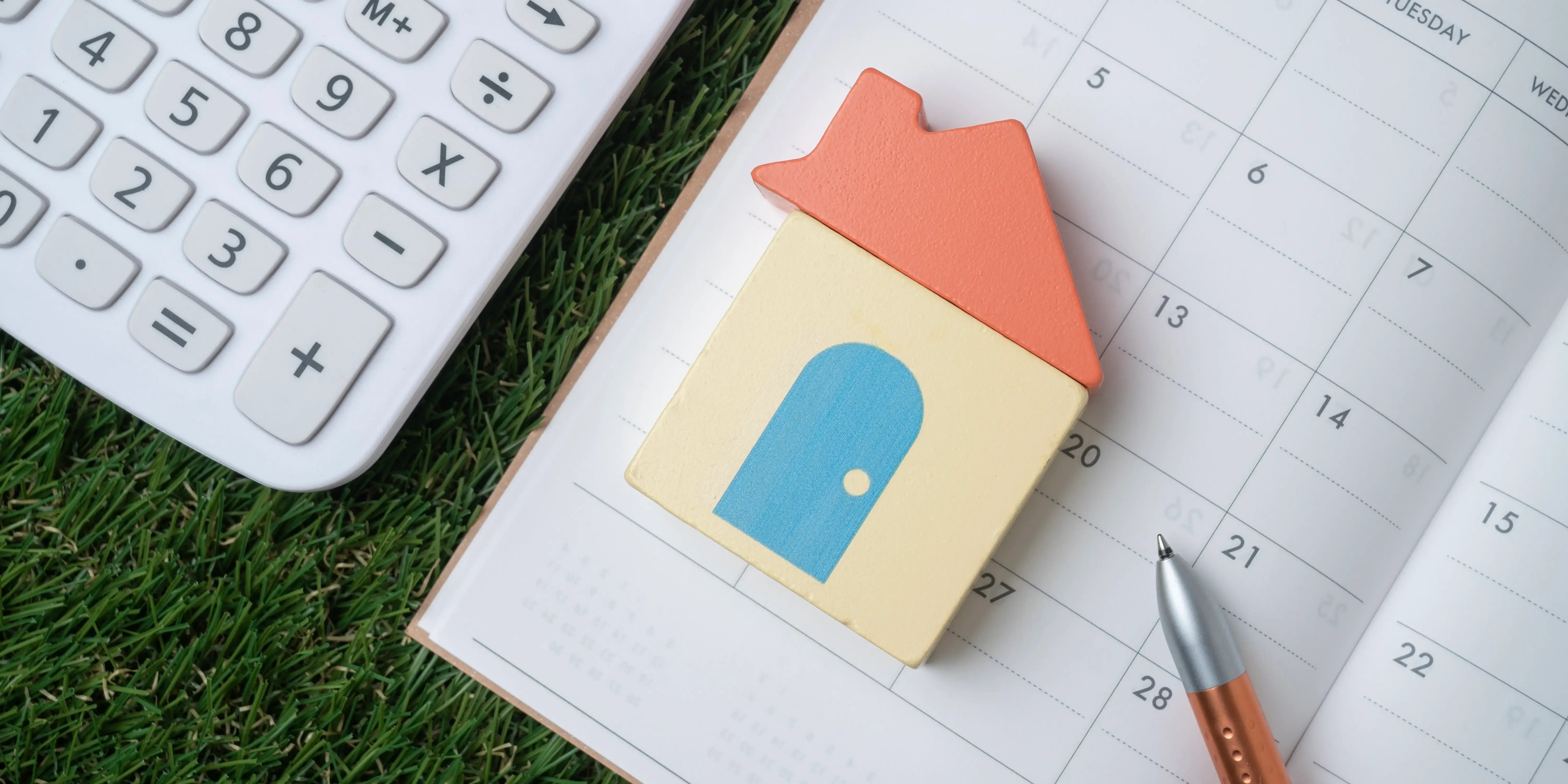 Una casa de madera, una agenda y una calculadora para calcular a cuántos años se paga una casa con crédito Infonavit