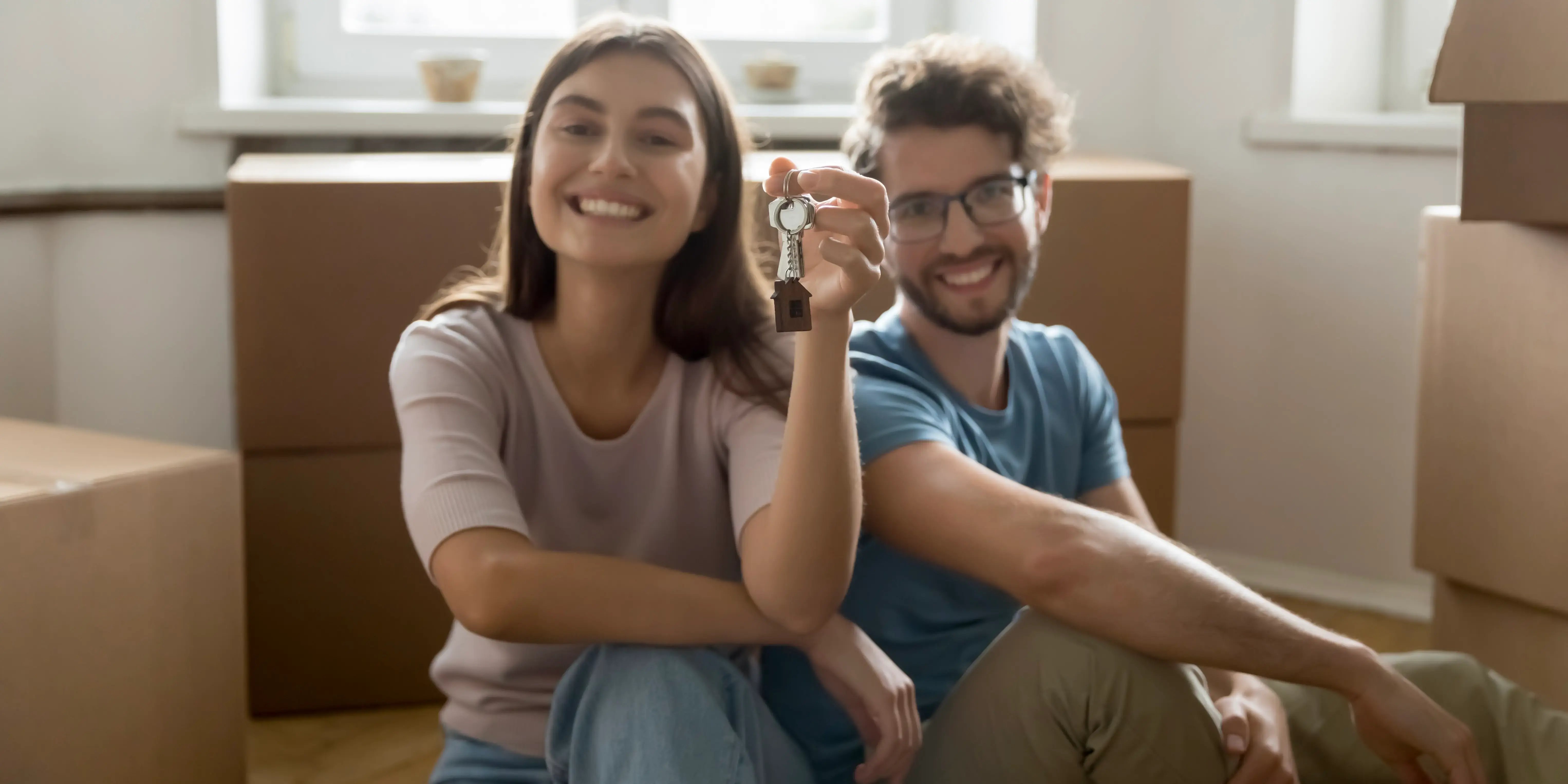 Una pareja joven sentada en el piso rodeada de un montón de cajas de cartón de la casa que acaban de comprar con su crédito FOVISSSTE
