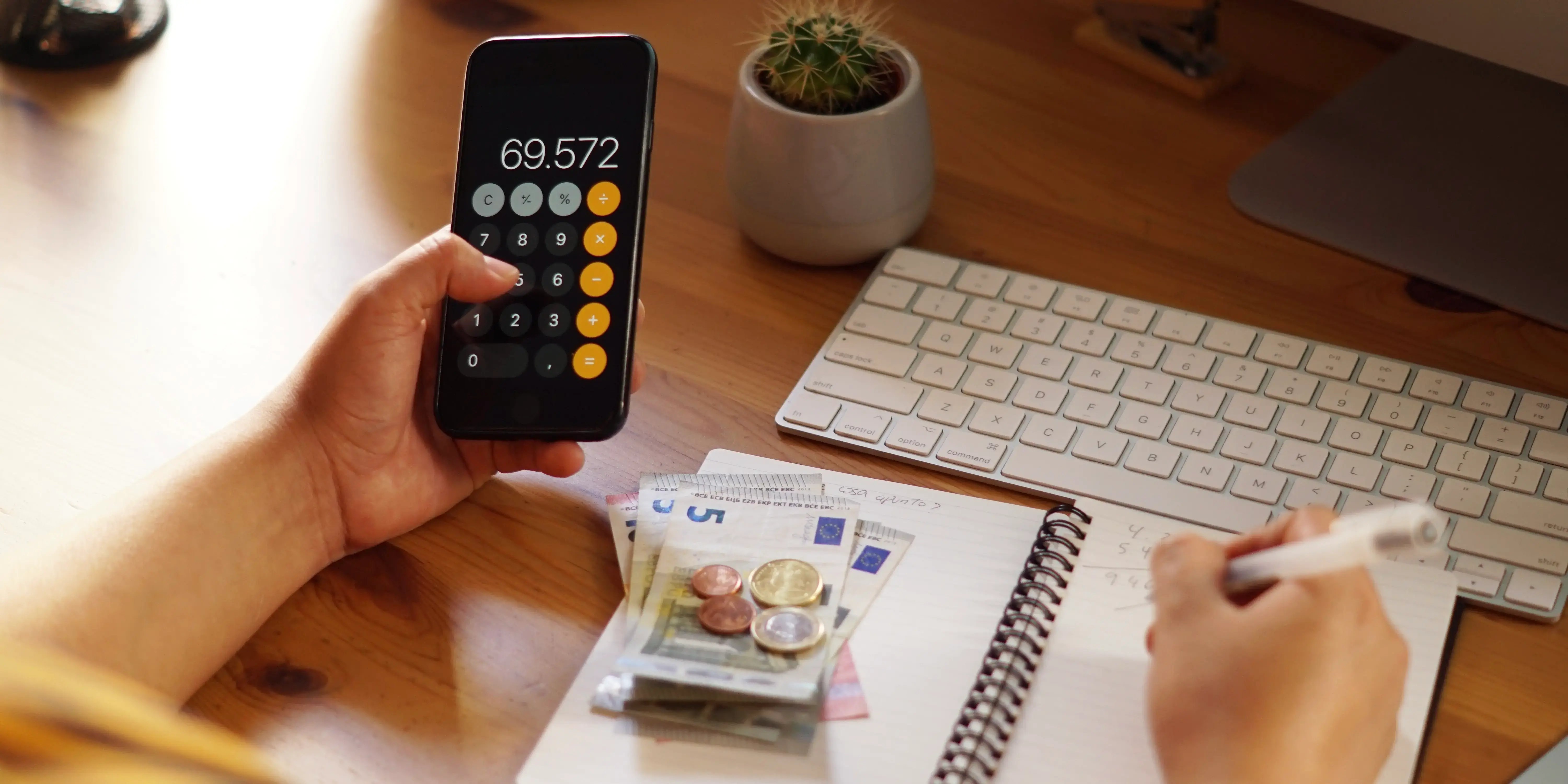 Persona sosteniendo un celular con calculadora, monedas y billetes. Mejorar tu historial crediticio