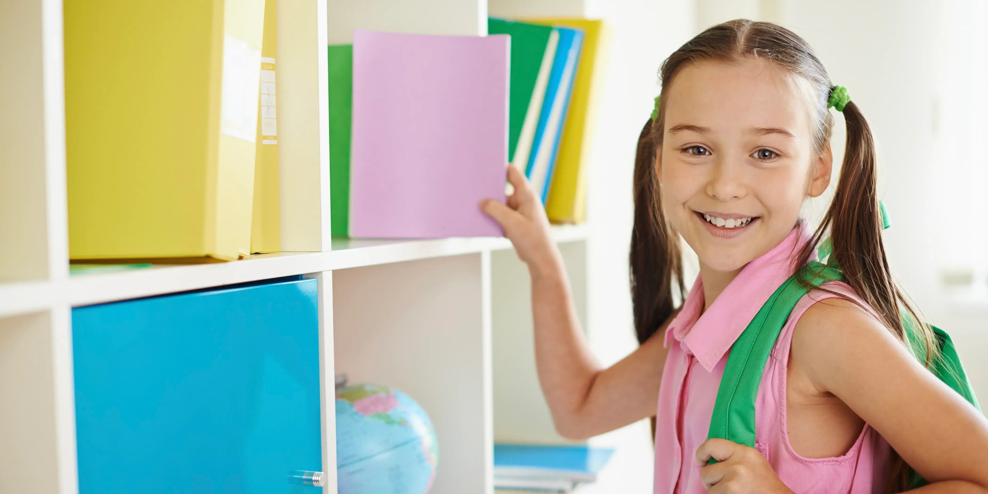 Niña con mochila y libros. Casa cerca de la escuela