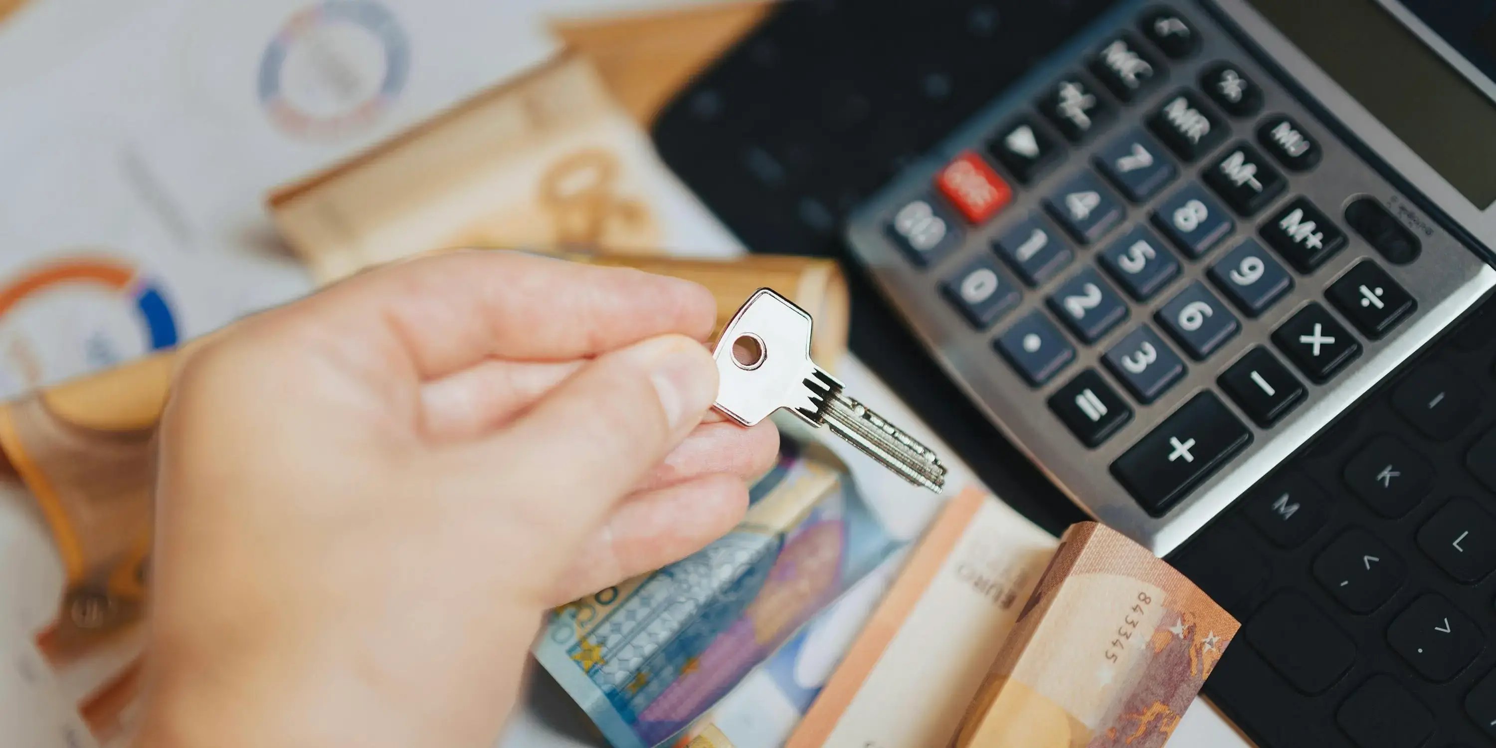 Mano sosteniendo llave con calculadora y billetes al fondo. Hipoteca 15 vs 30 años