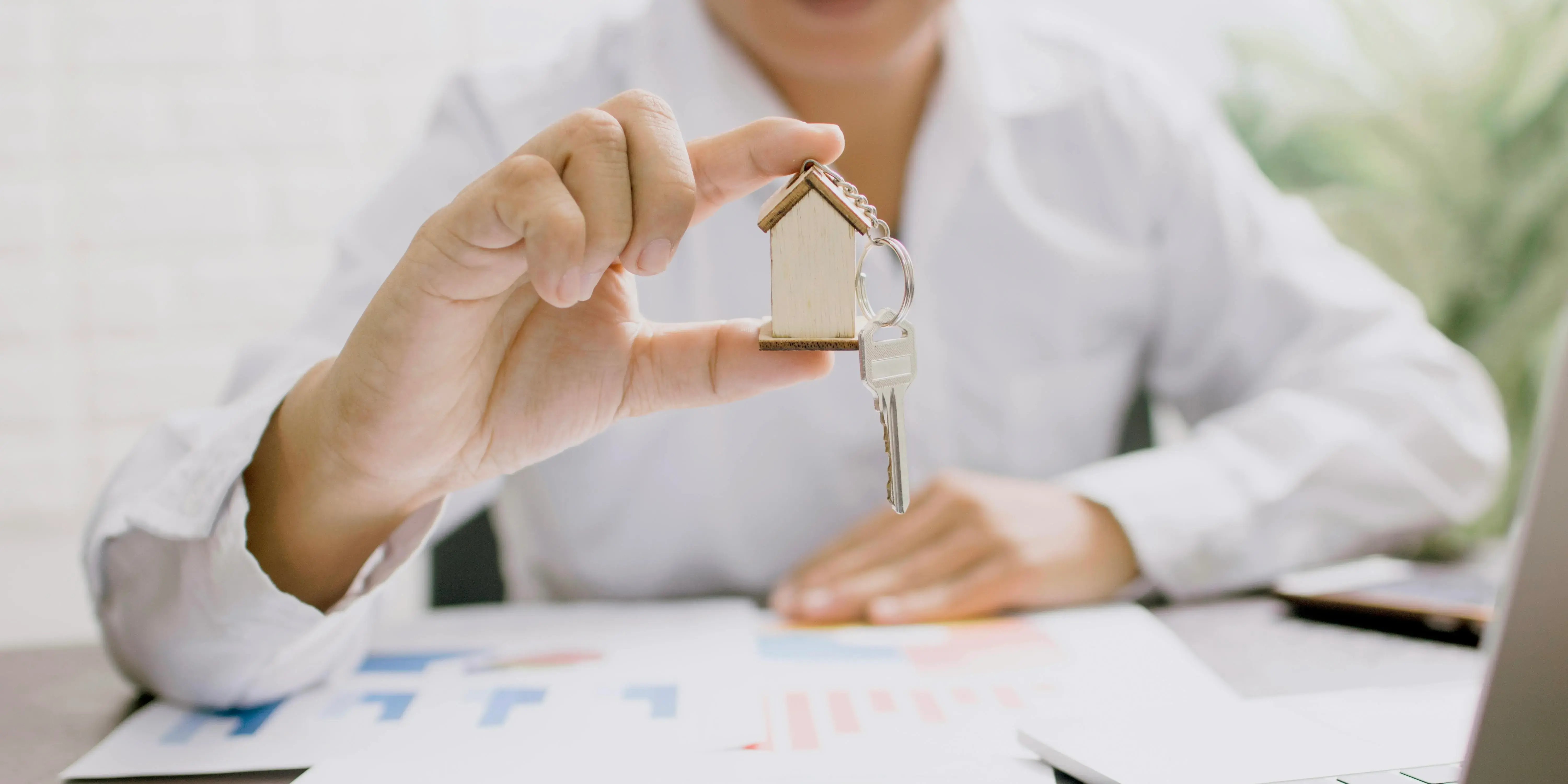 Persona sosteniendo llaves y con gráficas en un escritorio. Tu casa antes de los 30