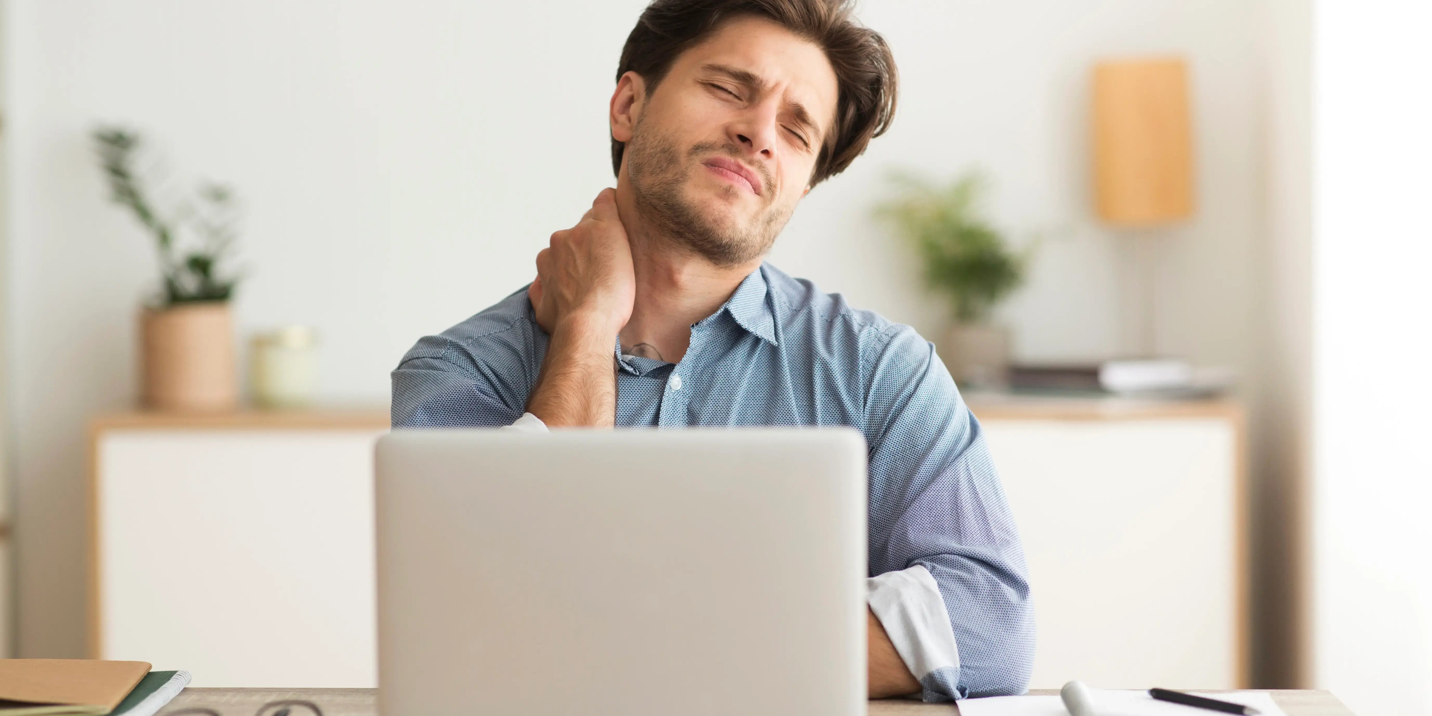 hombre en computadora agarrándose el cuello. ¿qué es sedentarismo?