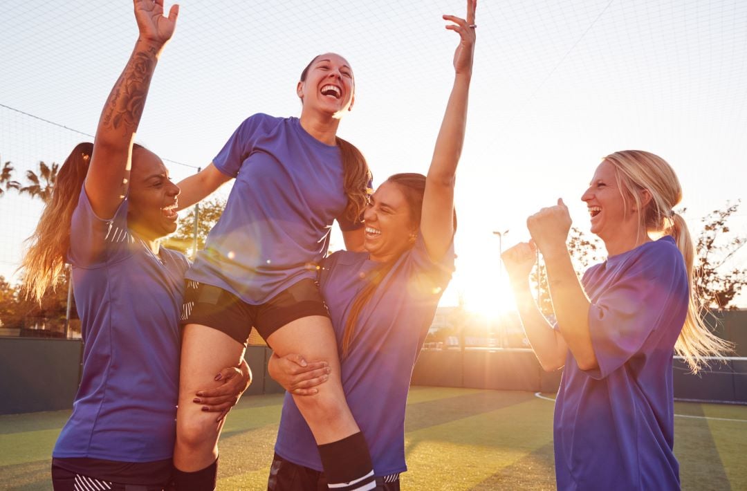Mujeres jugadoras de fútbol femenil celebrando en una cancha de fútbol.