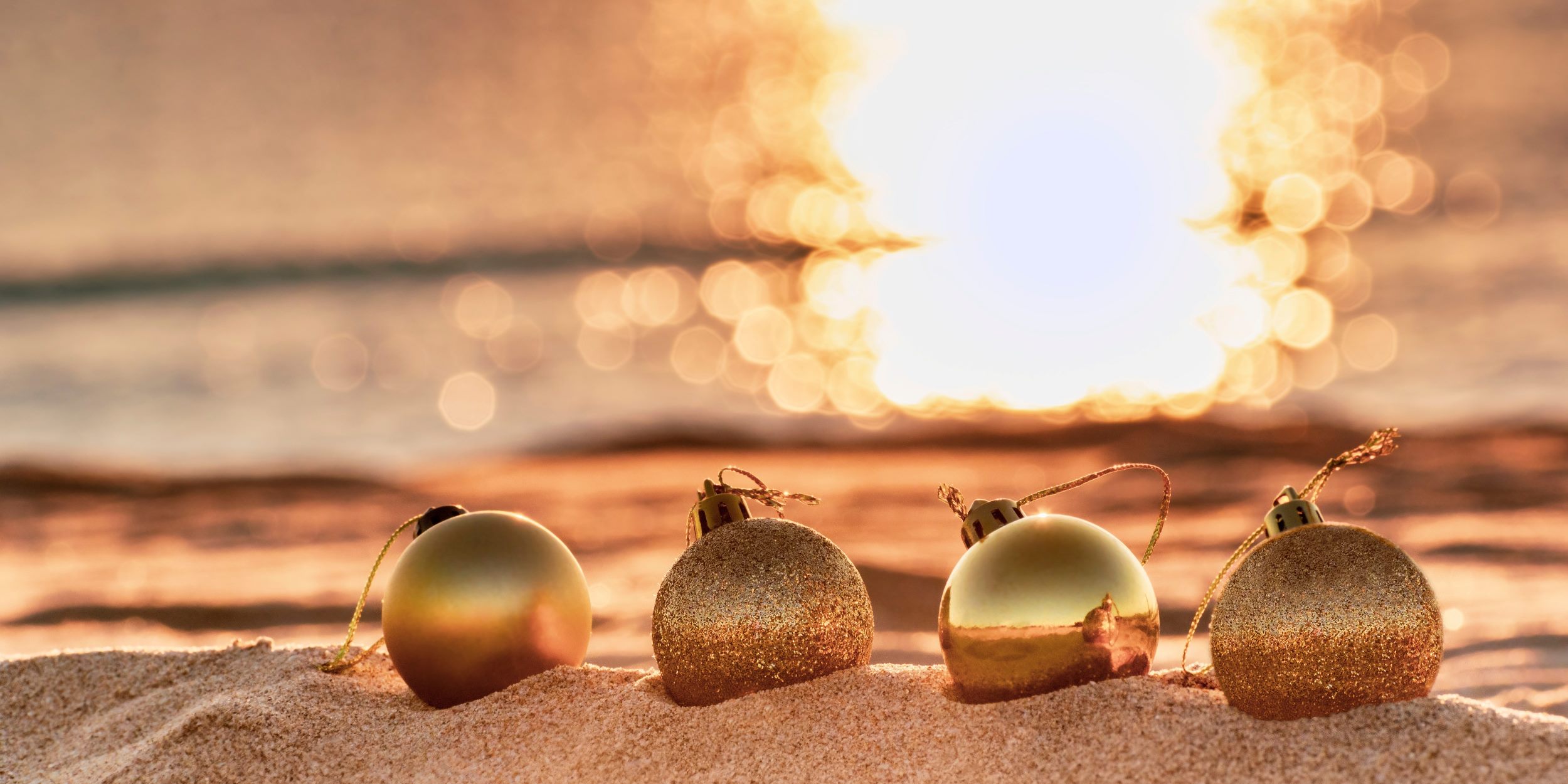 Esferas de Navidad en la costa. Están frente al mar en un atardecer. Representa la Navidad en la playa.