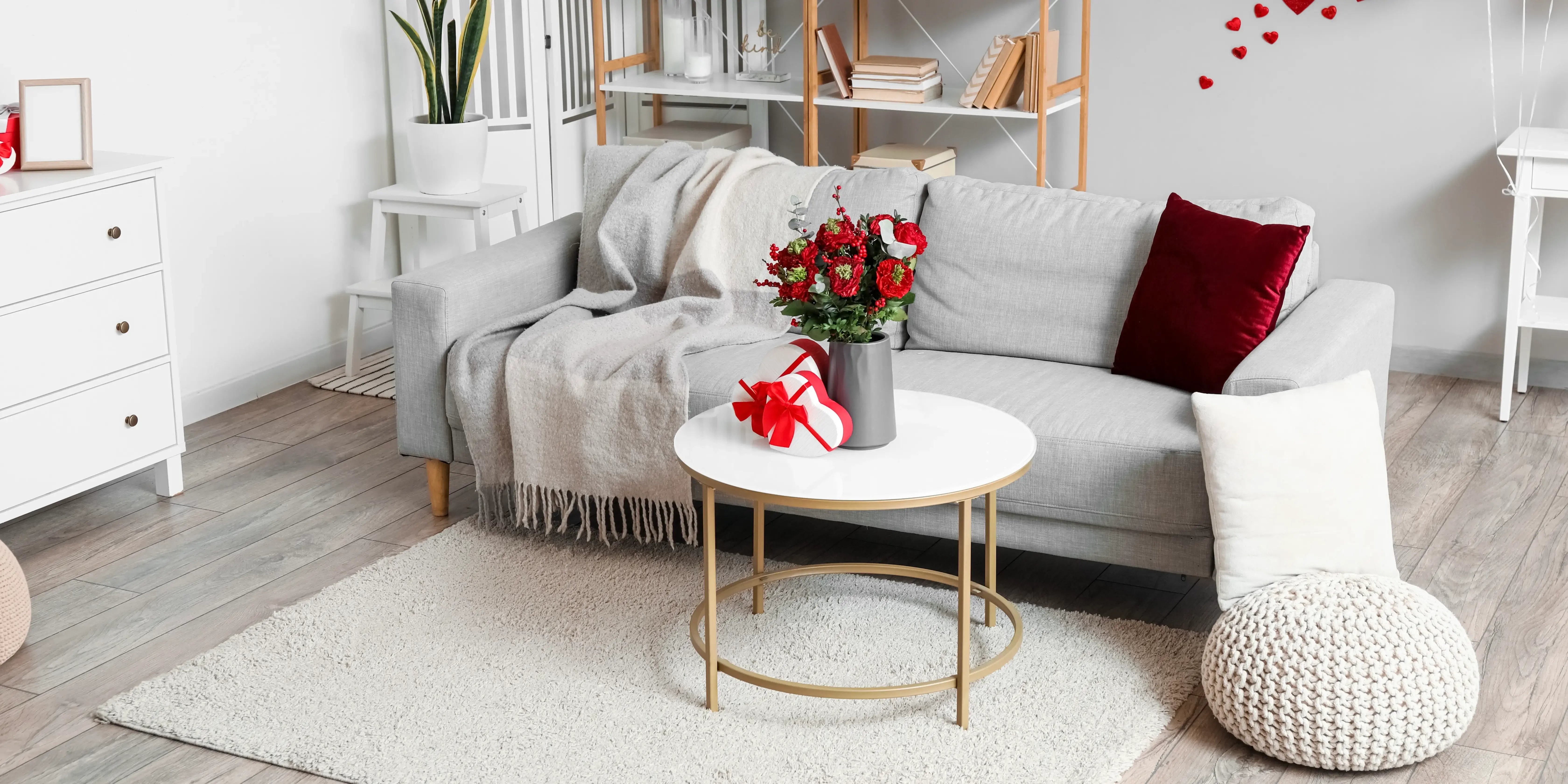 Mesa con arreglo floral y sillón con manta y cojín rojo. Decora tu departamento San Valentín