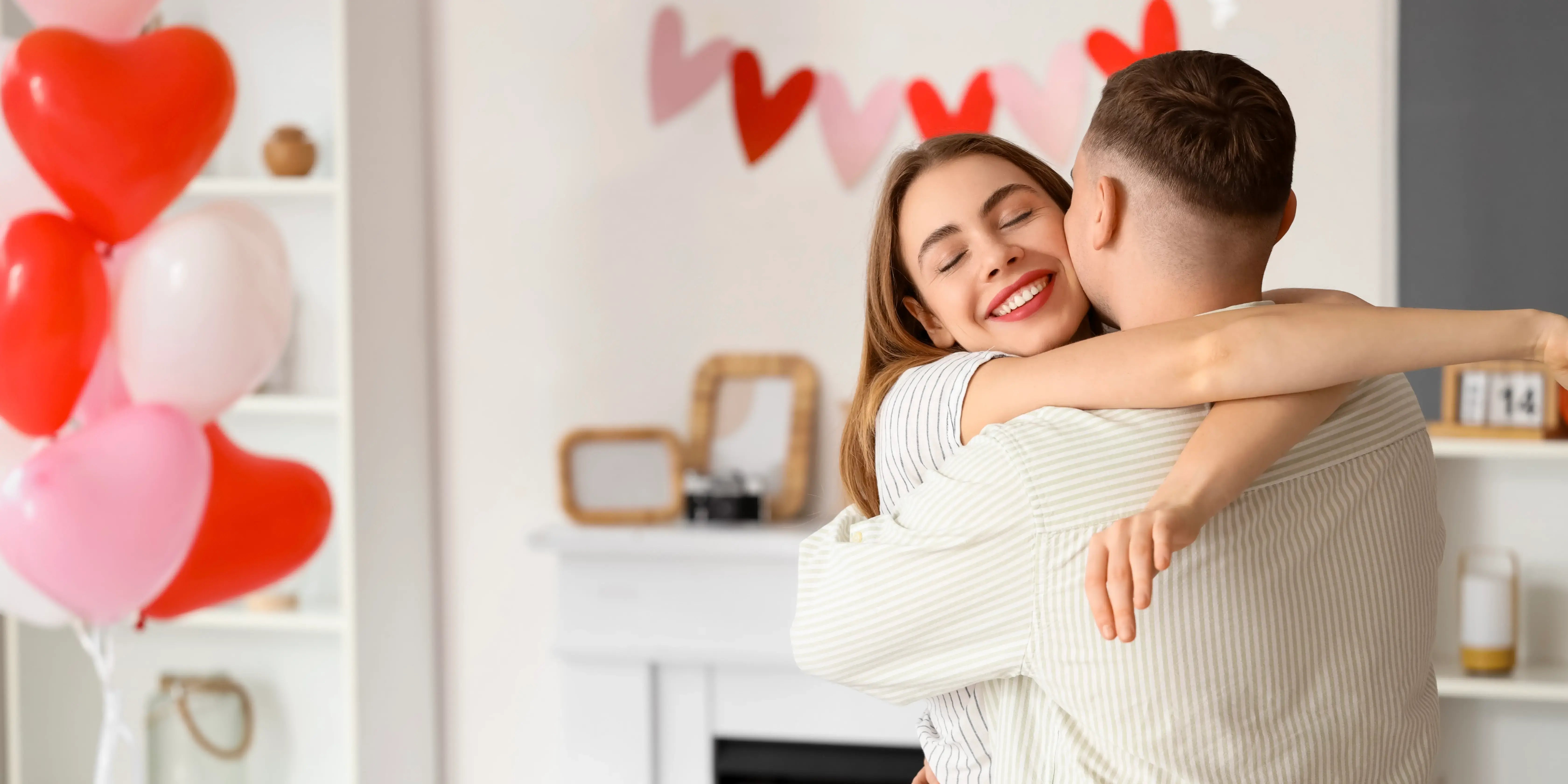 Pareja abrazándose, y globos de corazón. San Valentín en casa