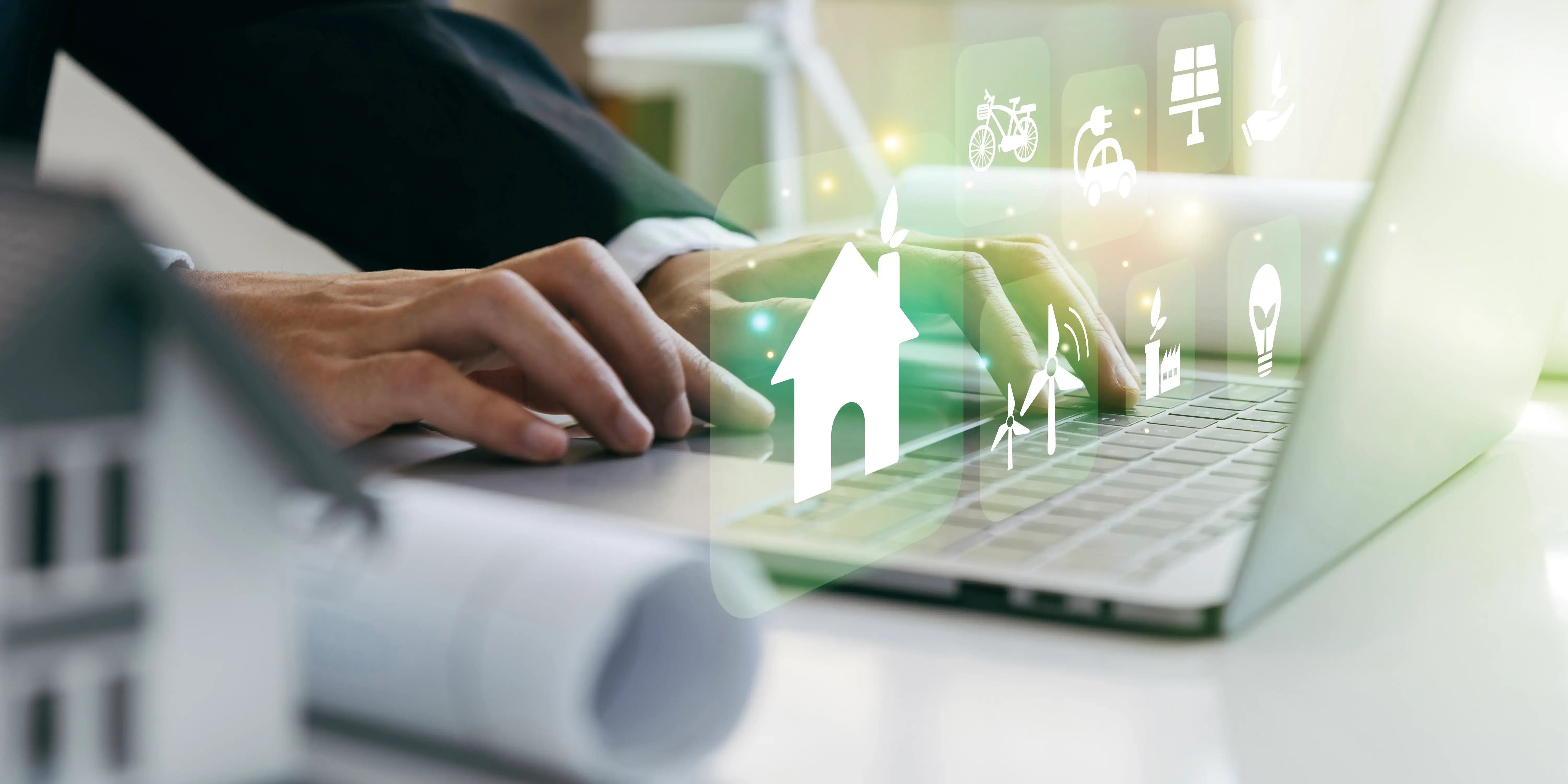 Hombre en computadora con planos y una maqueta de una casa. Desarrollo sustentable