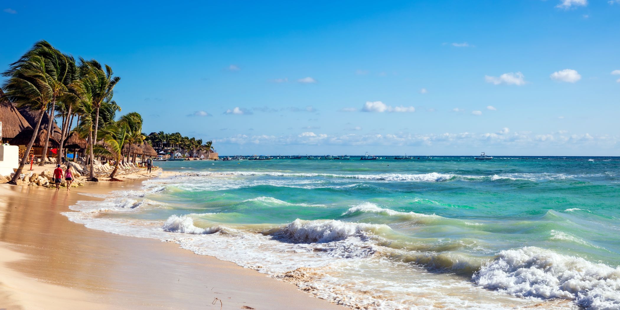 Playa del Carmen, México. Hay olas y mar color turquesa, arena, palmeras y personas.