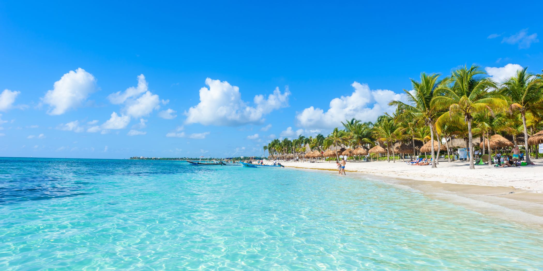 Playa de Cancún, en la Riviera Maya. Palmeras, nubes, arena y personas disfrutando el buen clima.